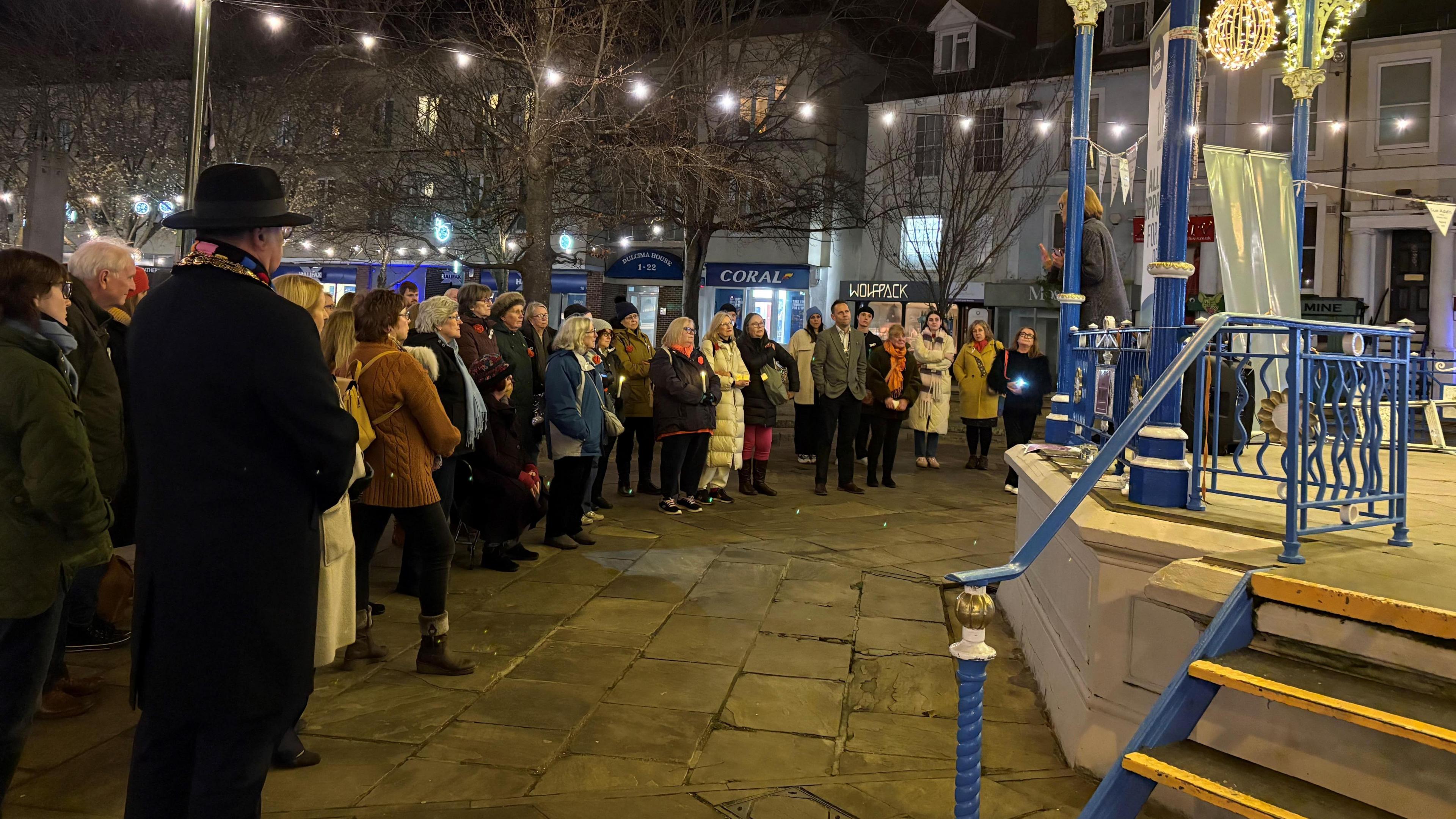 A group of men and women stand at a vigil at Horsham bandstand 