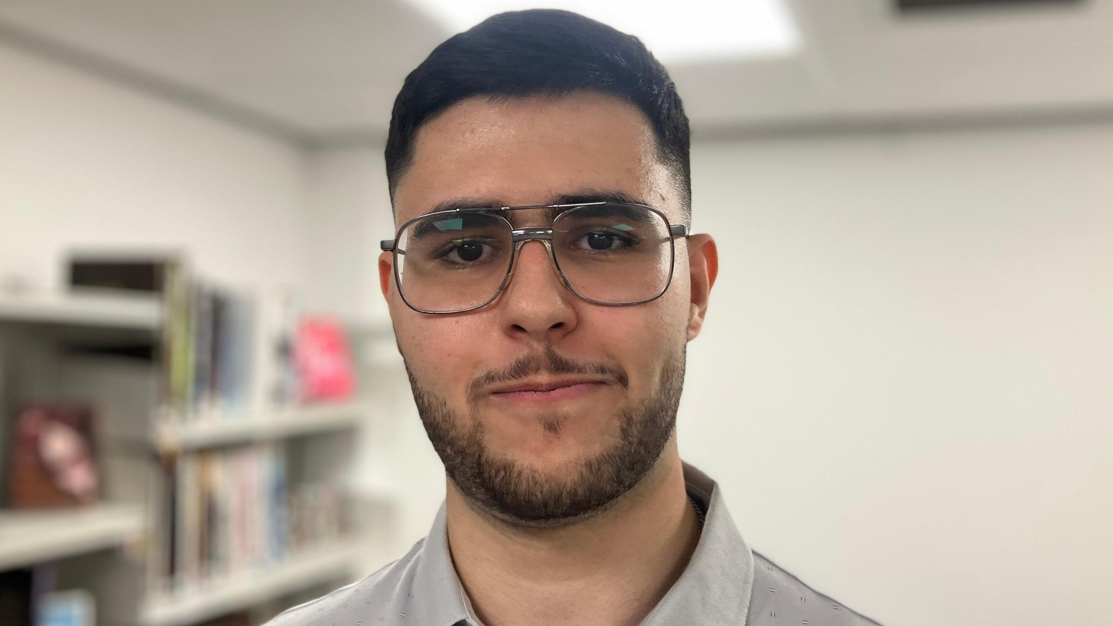 A man with dark hair and glasses wearing a grey shirt
