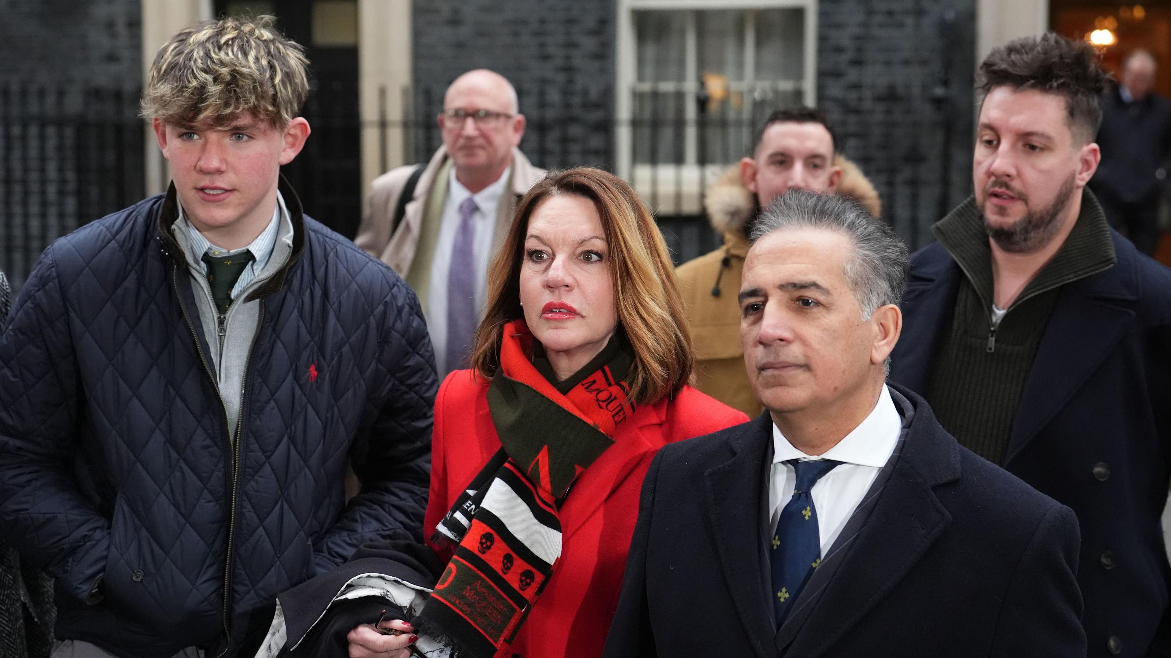 The families of the Nottingham attacks victims outside No 10 Downing Street. Charlie Webber is wearing a navy quilted jacket, standing next to Emma Webber wearing a red coat and Sanjoy Kumar wearing a tailored wool coat. They are standing in front of Ian Coates's sons James and Lee.  