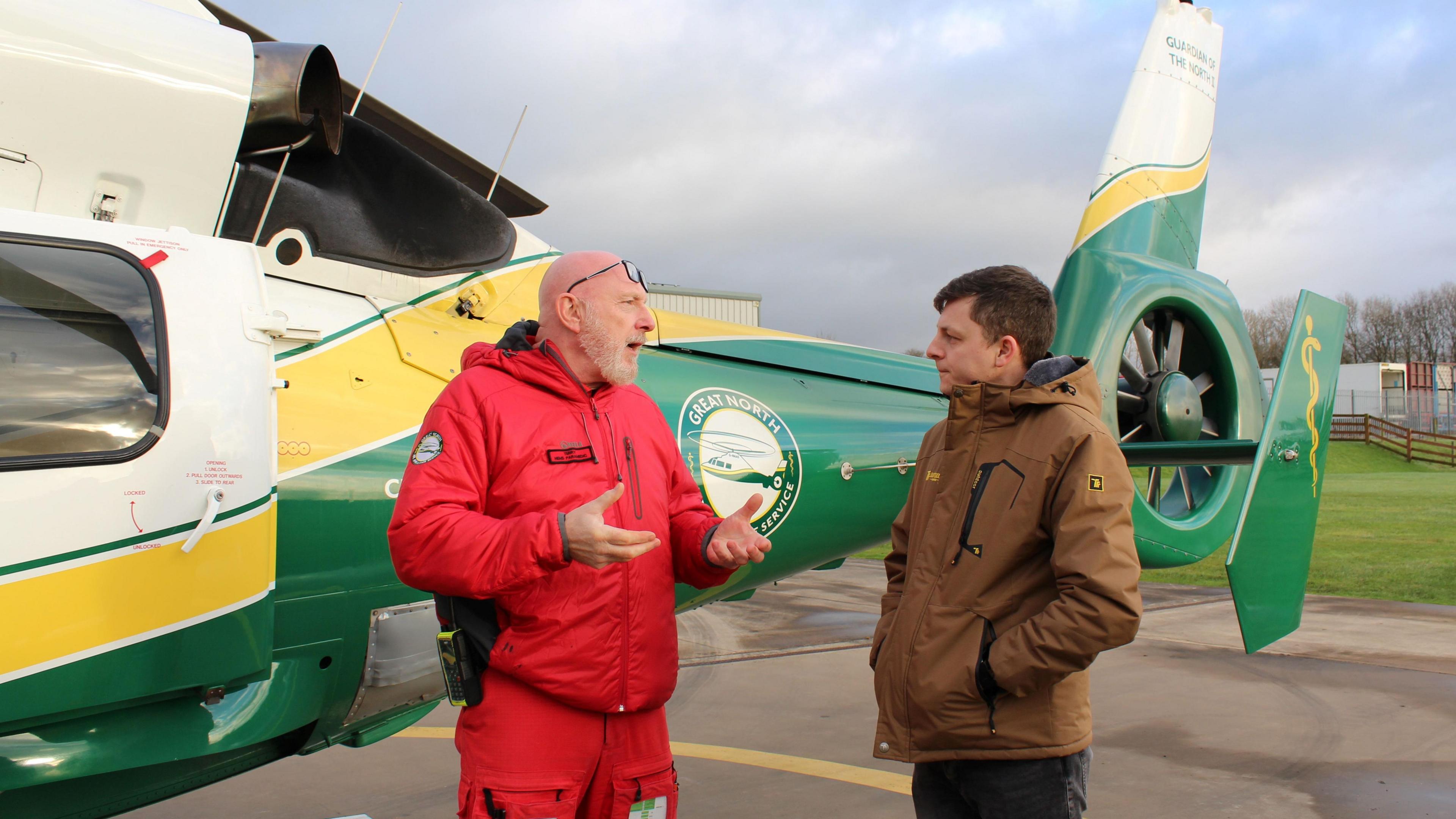 Paramedic Terry Sharpe and Jed Rayner talking to each other in front of a GNAAS helicopter. 