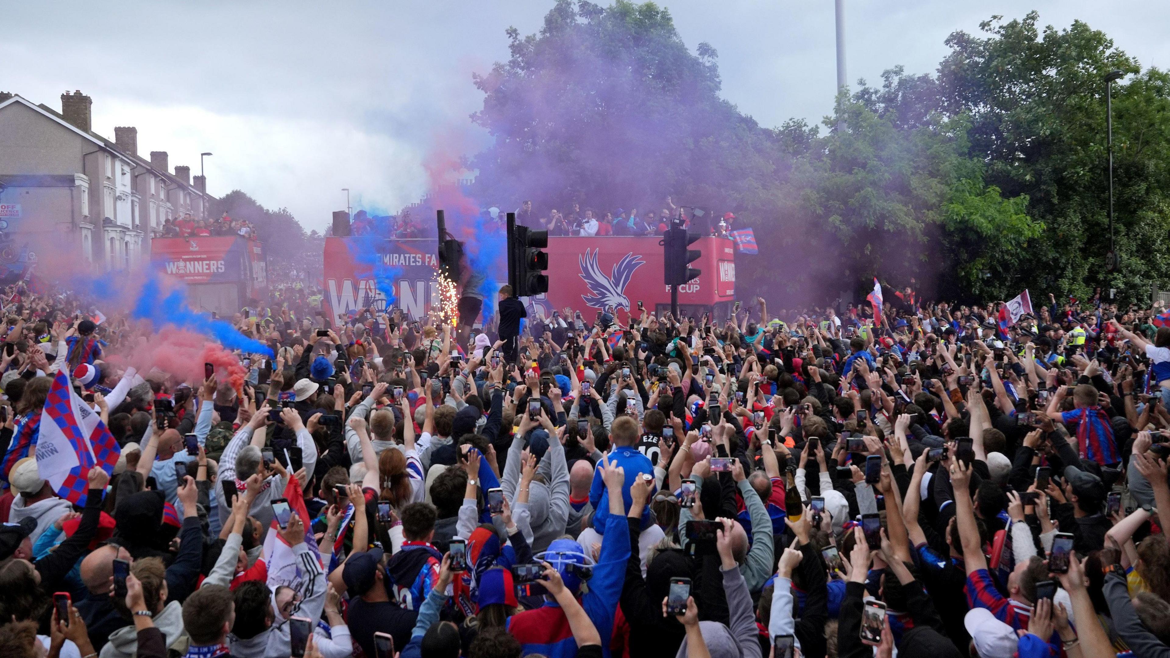 Crowds of fans wearing red and blue and an open top bus on side view carrying the team