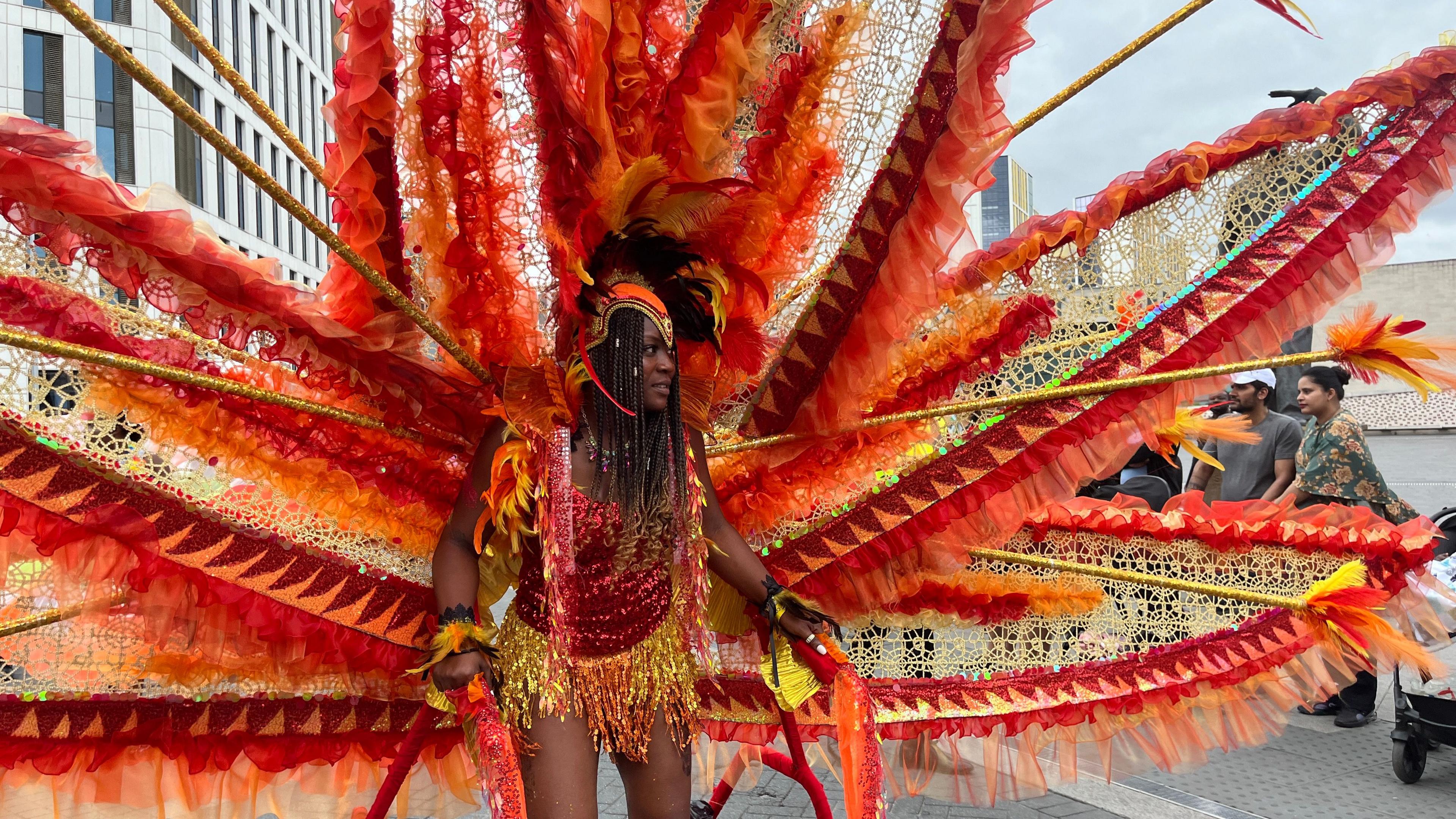 A female performer in an ornate feathered costumeand bright clothing during a Caribbean festival parade