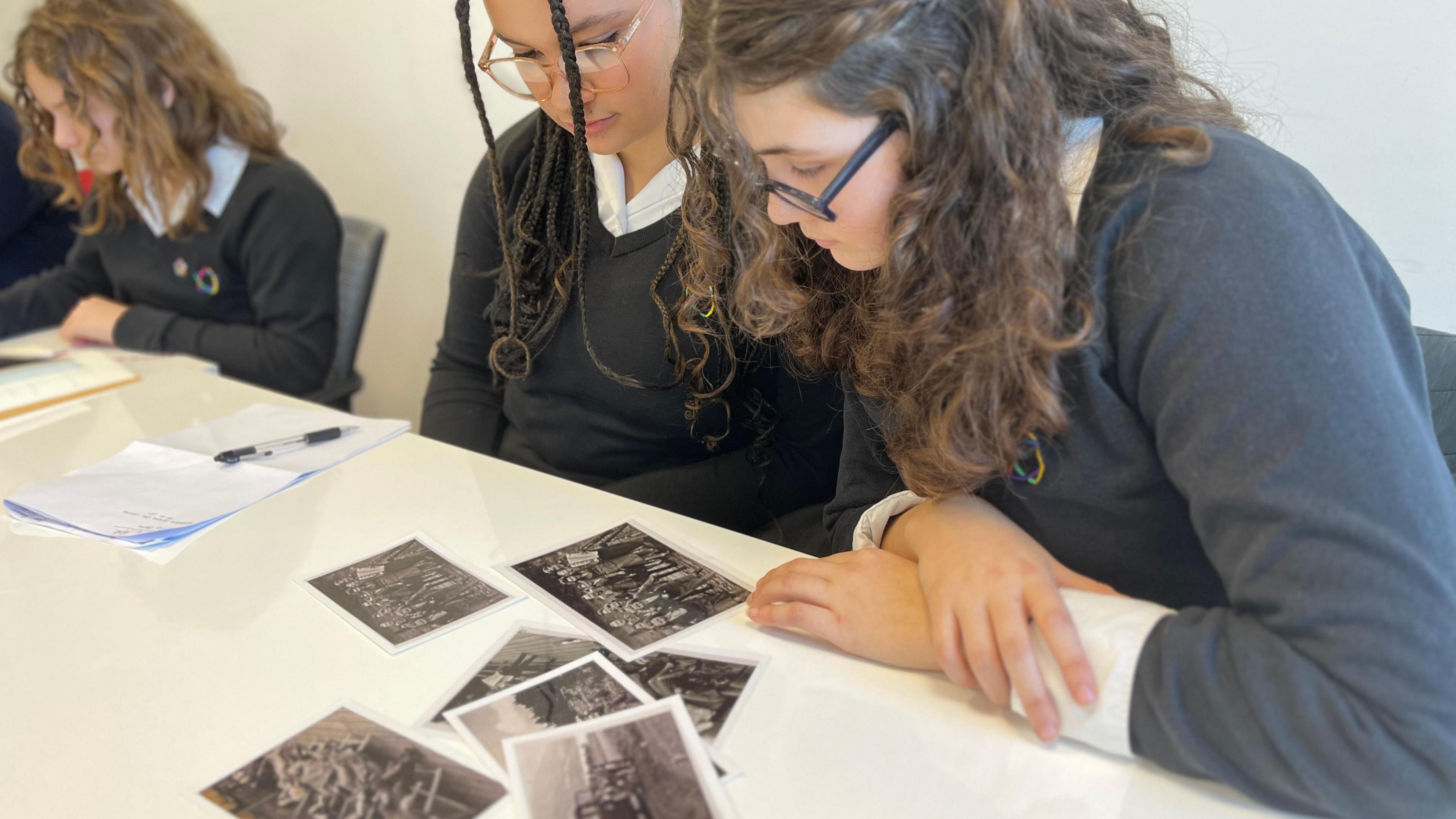 School students sat at a desk looking at black and white photographs.