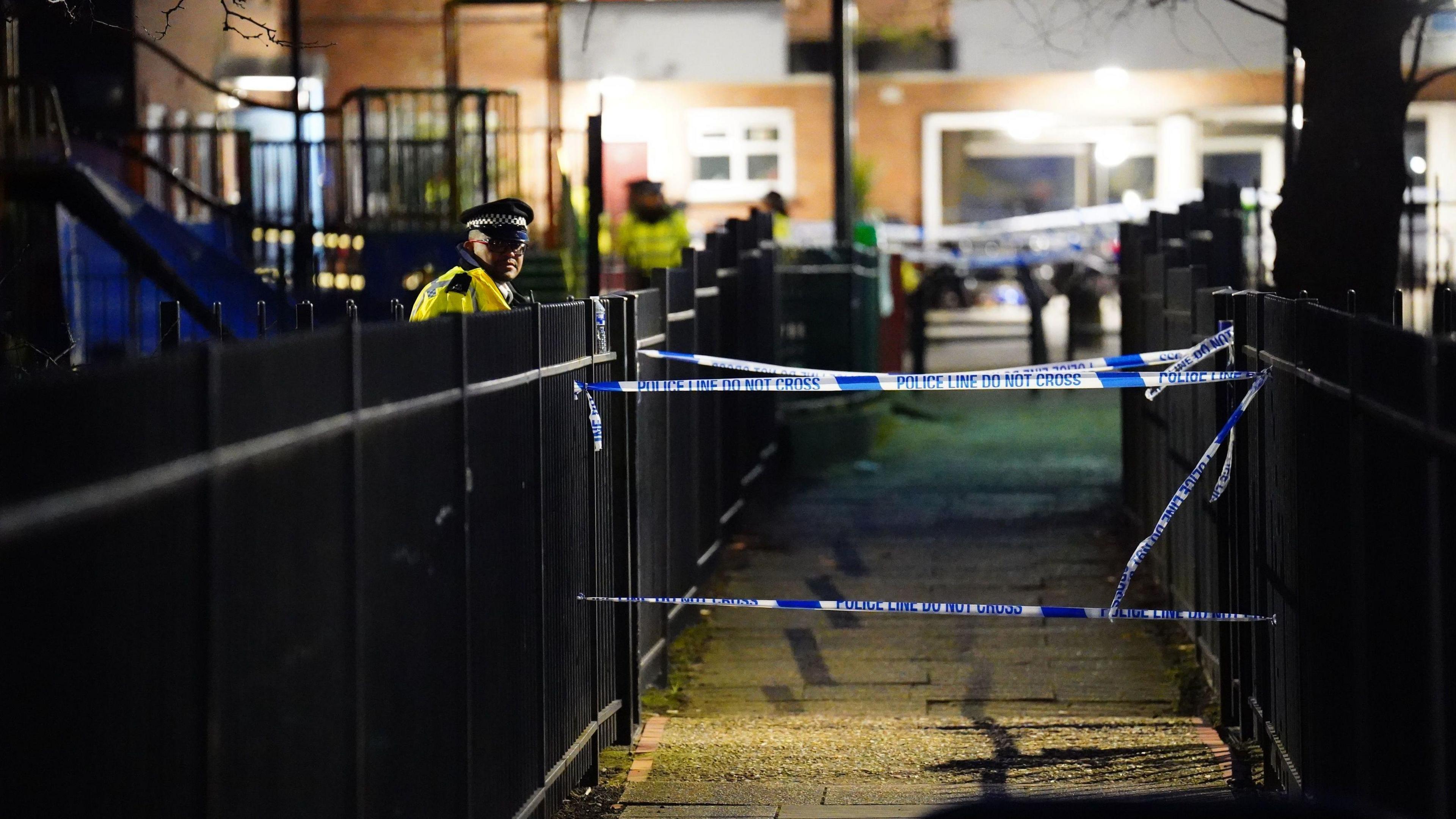 A night shot of the police cordon and police officers standing on one side of a black gate.