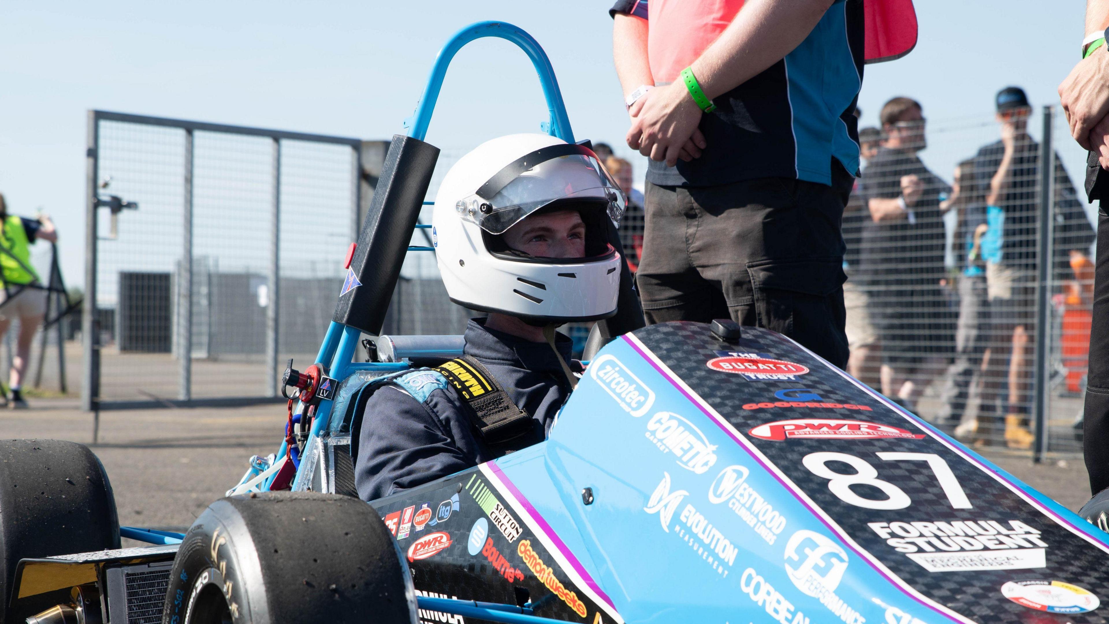 Driver in white helmet sitting in blue racing car