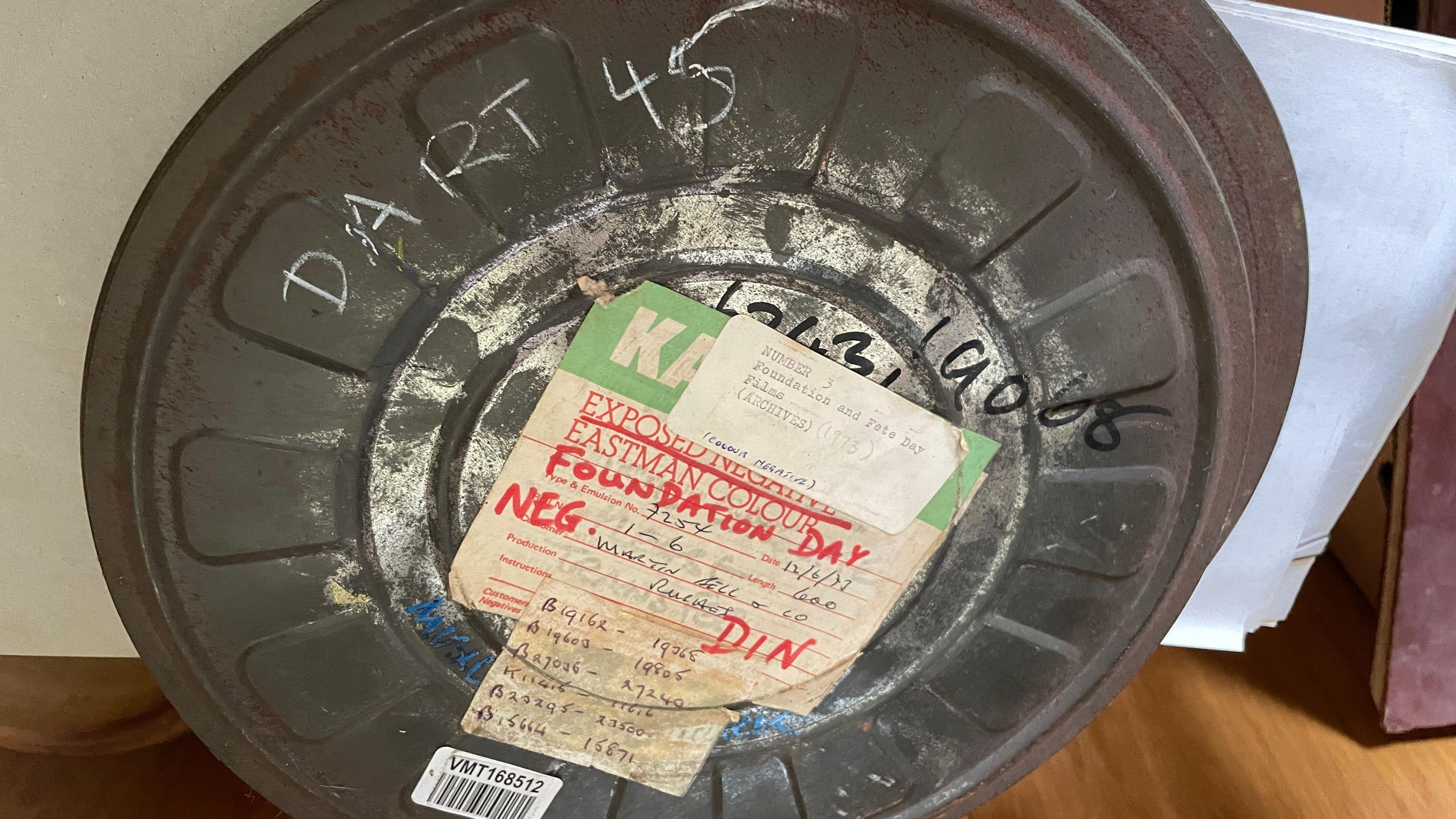 The photo shows an old, round metal film canister with a paper label on it. Dart 45 is written across it in chalk.
