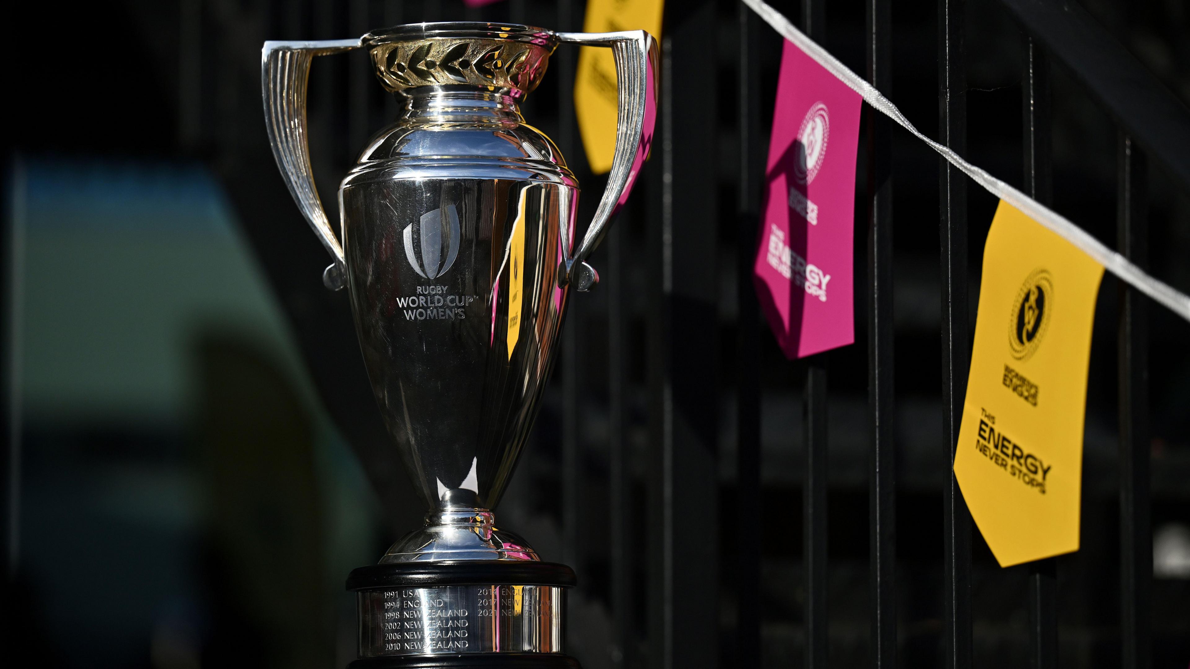 A photo of a shiny silver trophy. In the background there are pink and yellow bunting to represent the women's rugby world cup