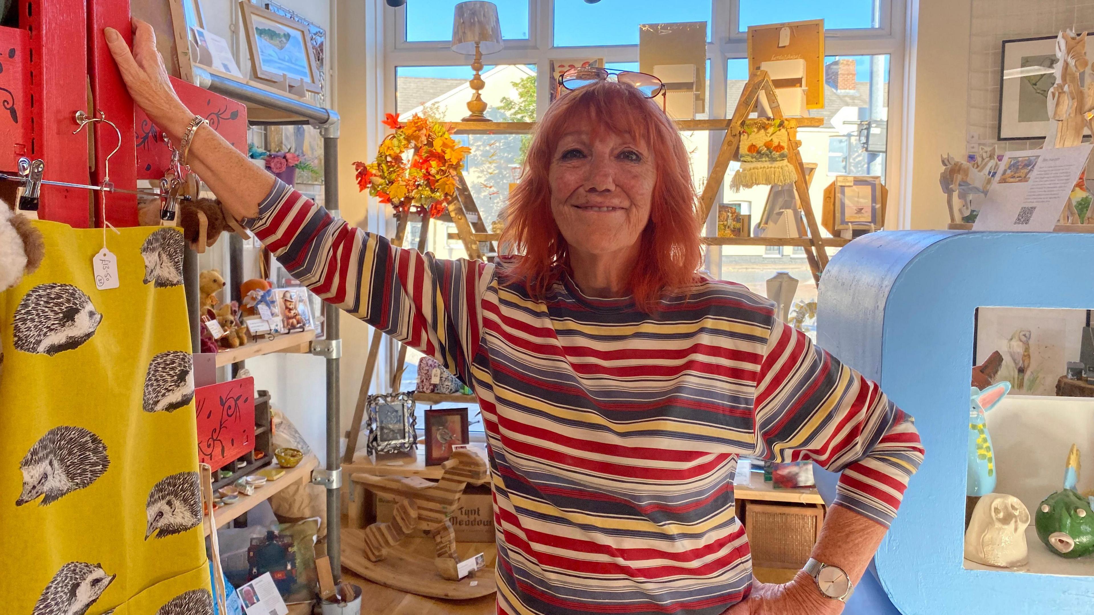 Wendy Culleton in a stripy jumper with her arm raised above her head as she leans on a pillar