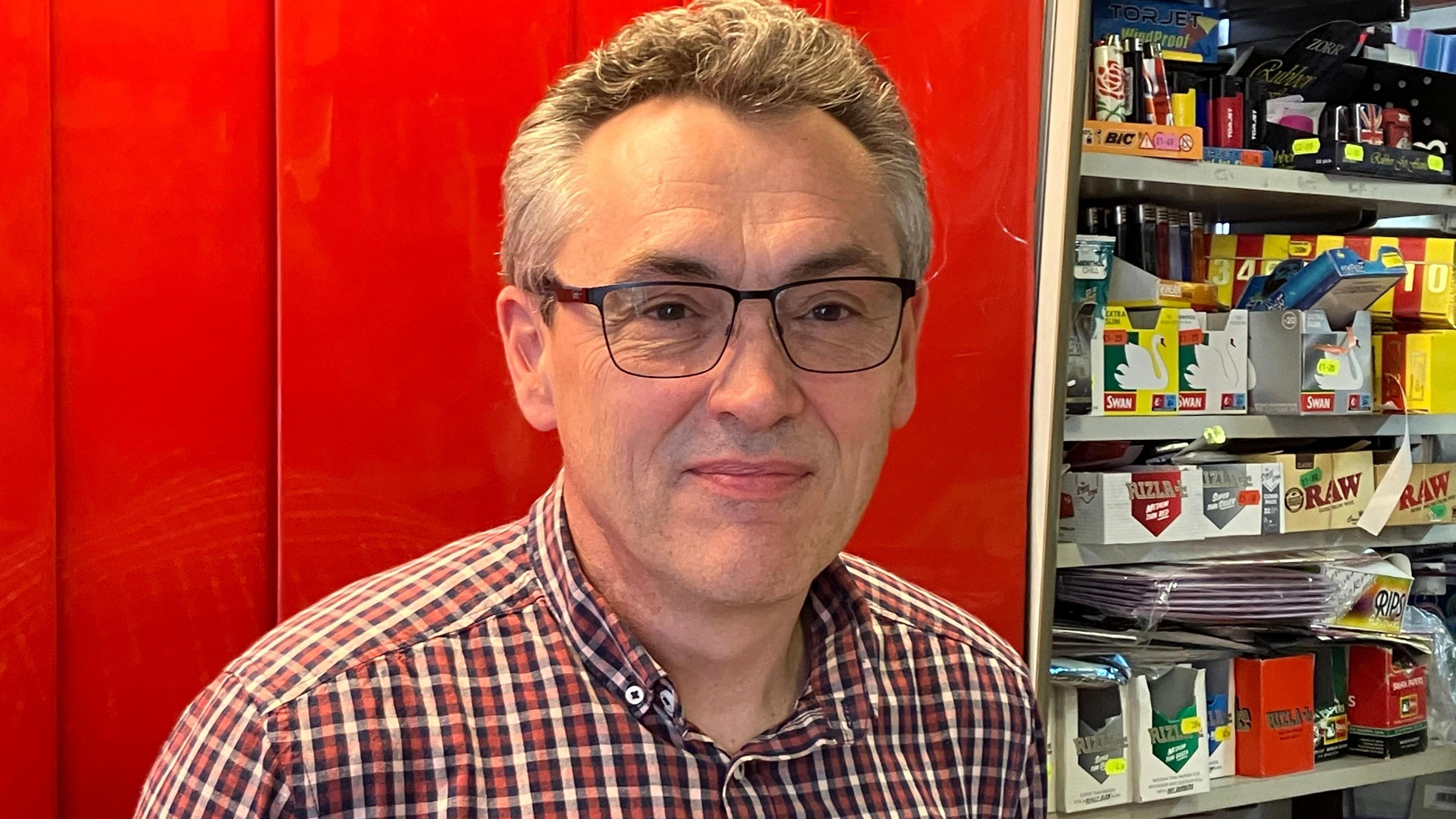 Shop keeper wearing glasses standing behind his counter