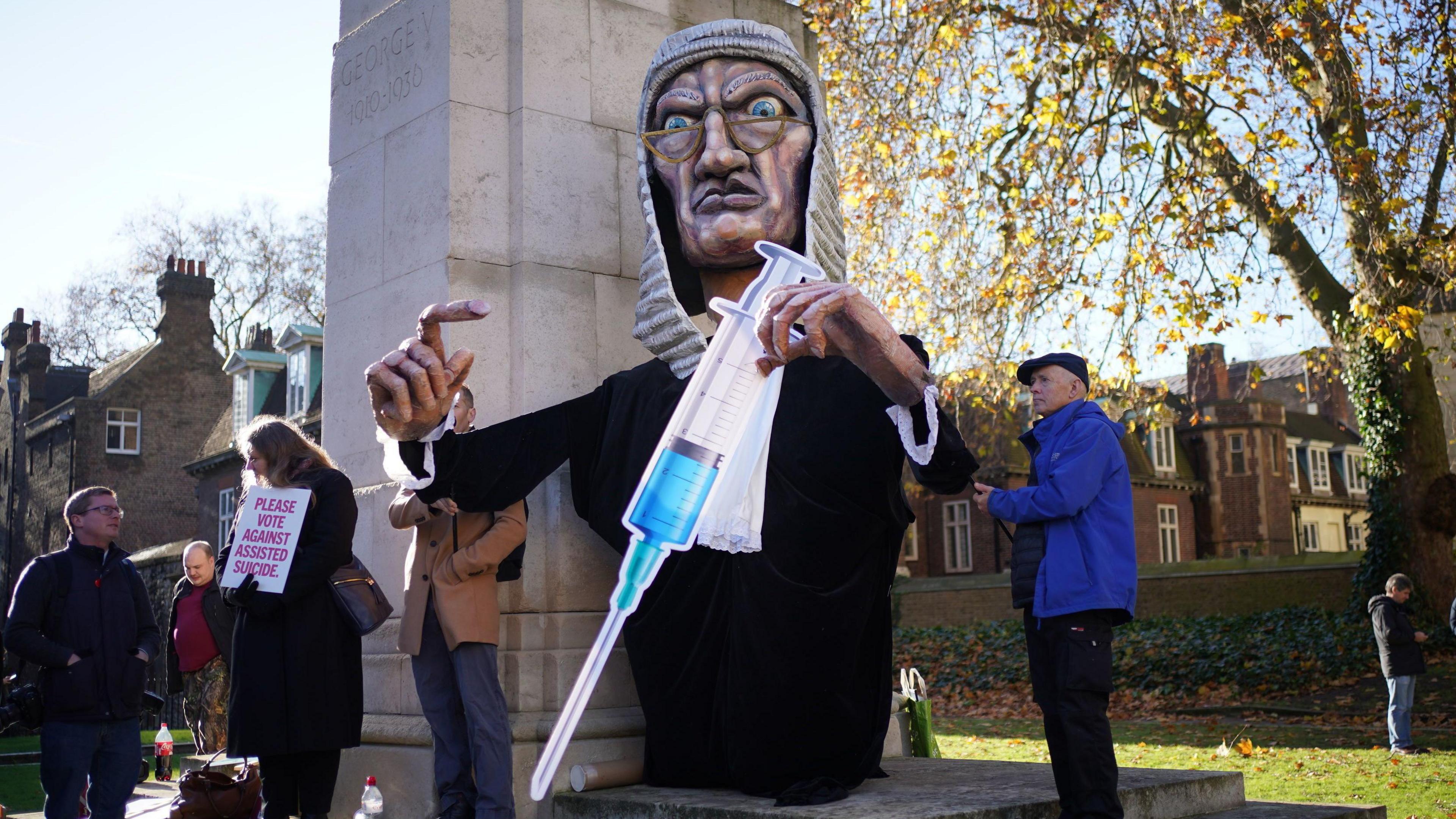 A large puppet judge holds a large syringe