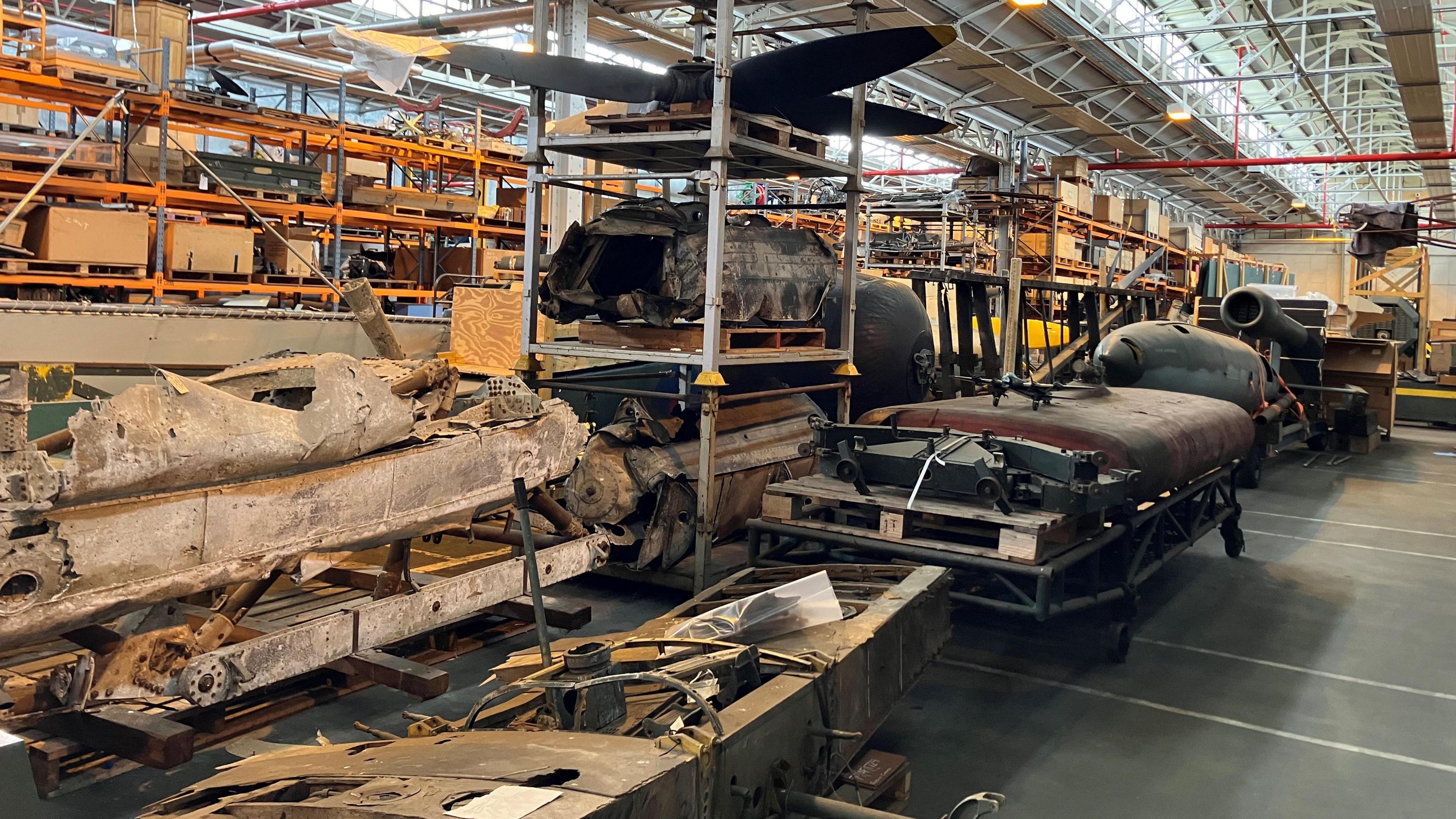 Large parts of vehicles on shelves or trolleys on the floor of a large warehouse.