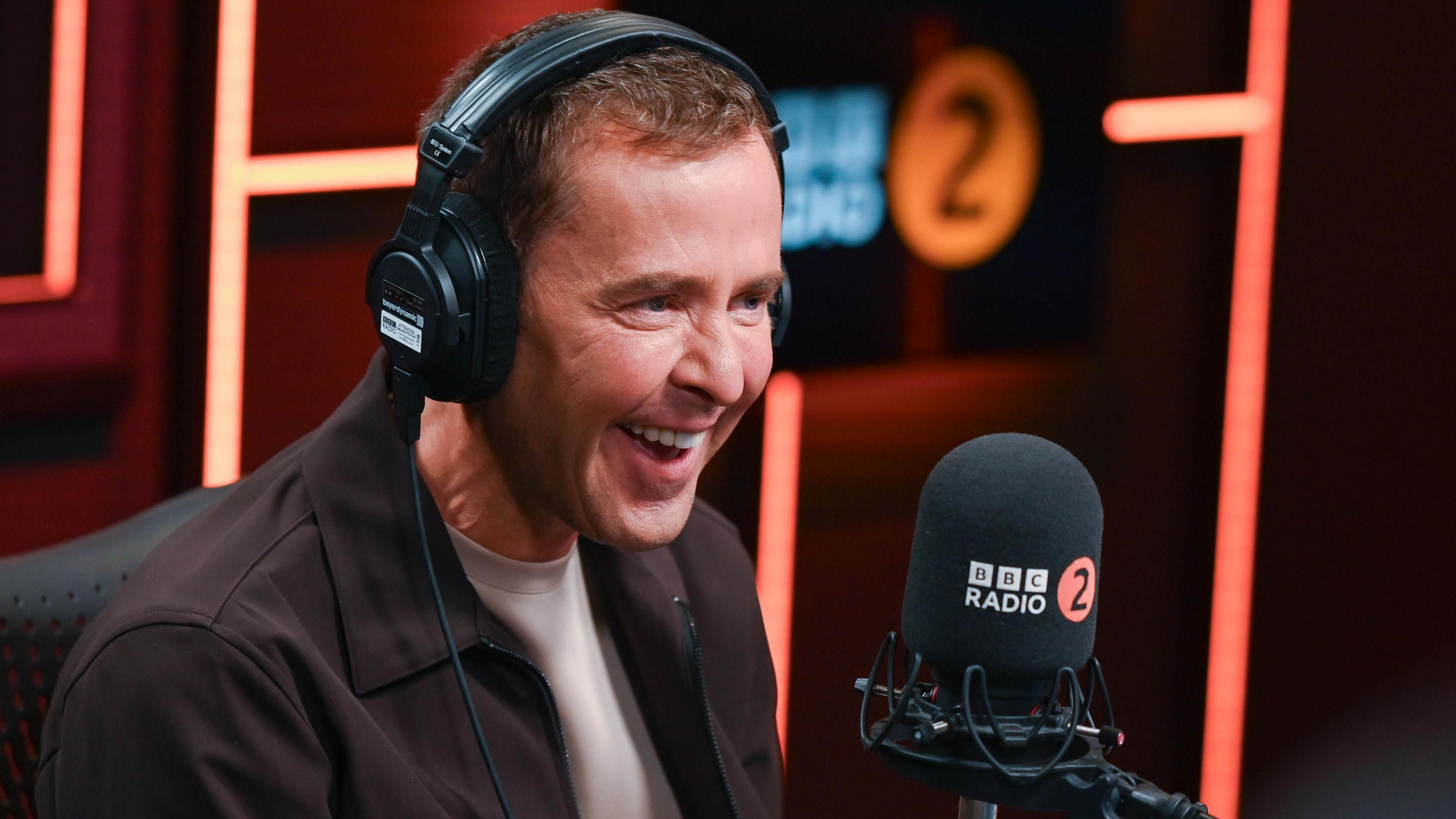 Presenter Scott Mills with headphones on in front of a microphone in the BBC Radio 2 Breakfast Show studio