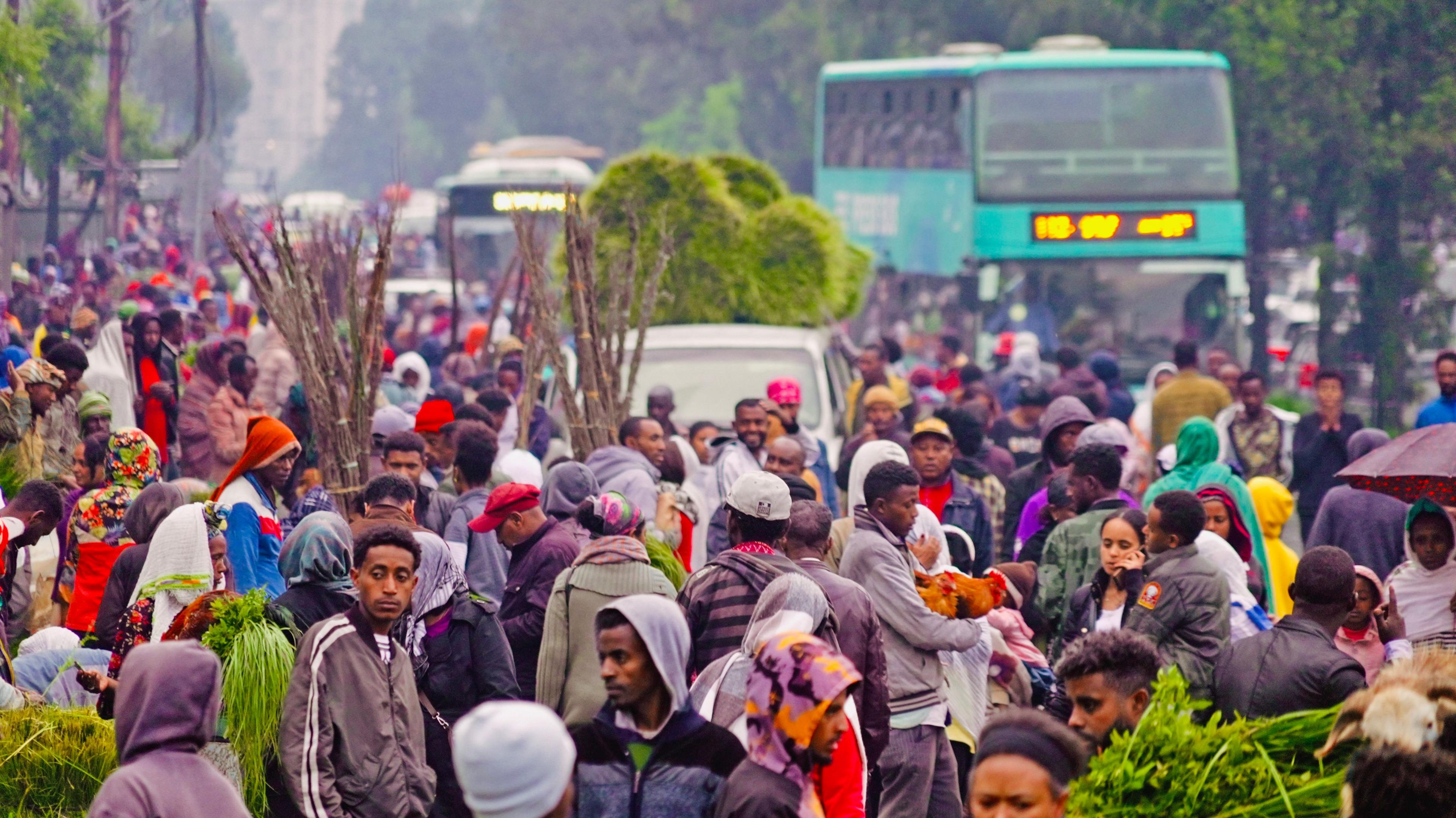Big crowds at a market in Ethiopia's capital, Addis Ababa. Some people can been seen holding chickens, others long grass used in New Year celebrations. On the street behind a green double decker bus can be seen - Wednesday 10 September 2025.
