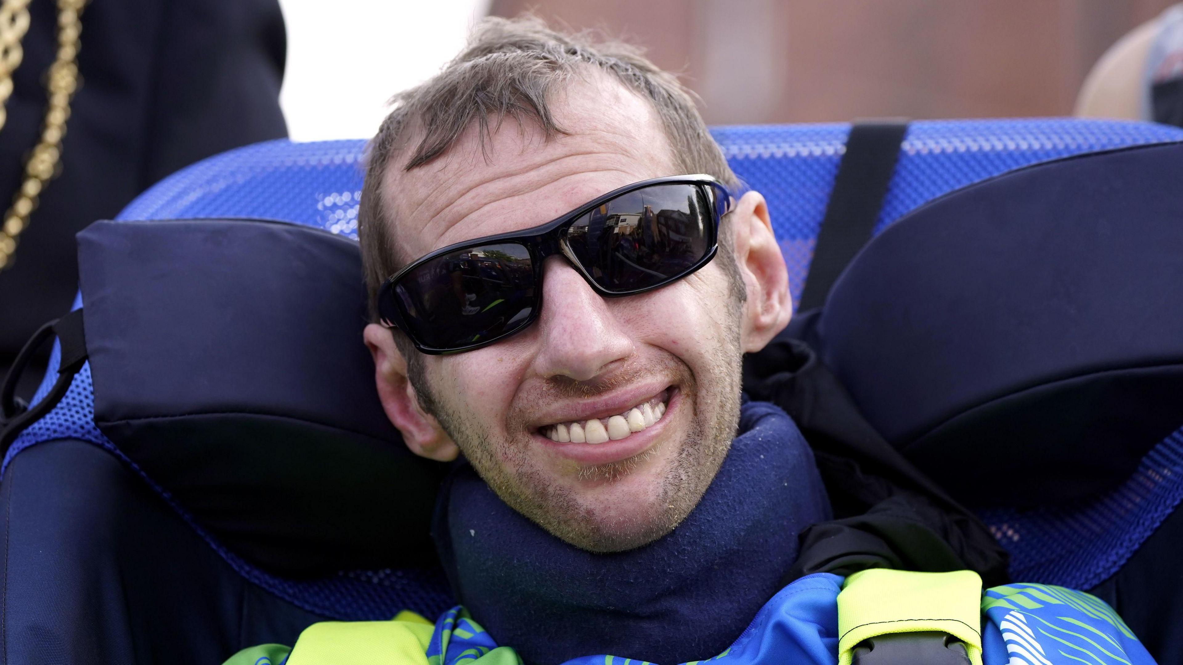 Rob Burrow CBE is pictured from the chest up, smiling at the camera and wearing sunglasses