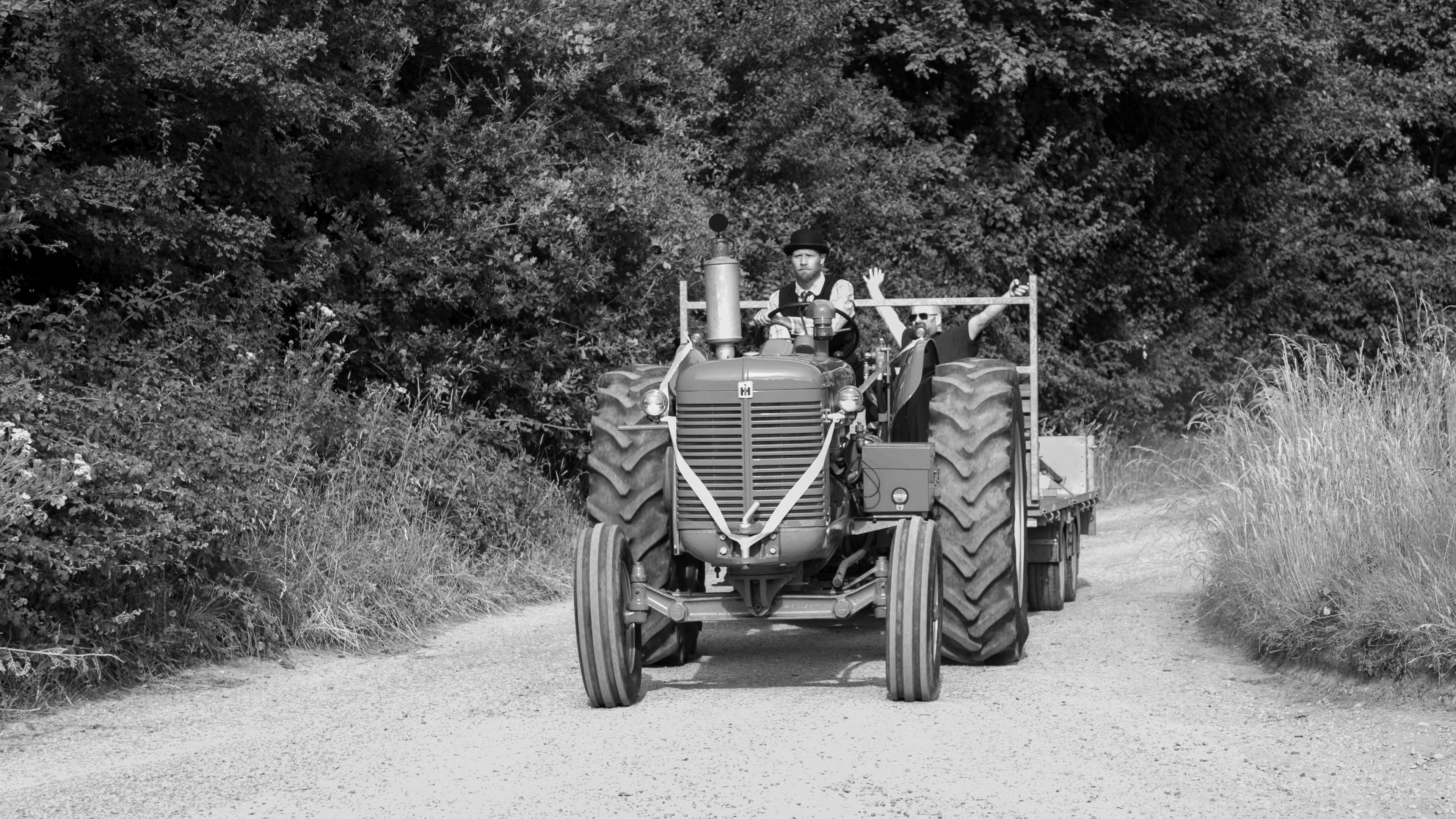 A black and white styled image of a tractor travelling on a dirt road