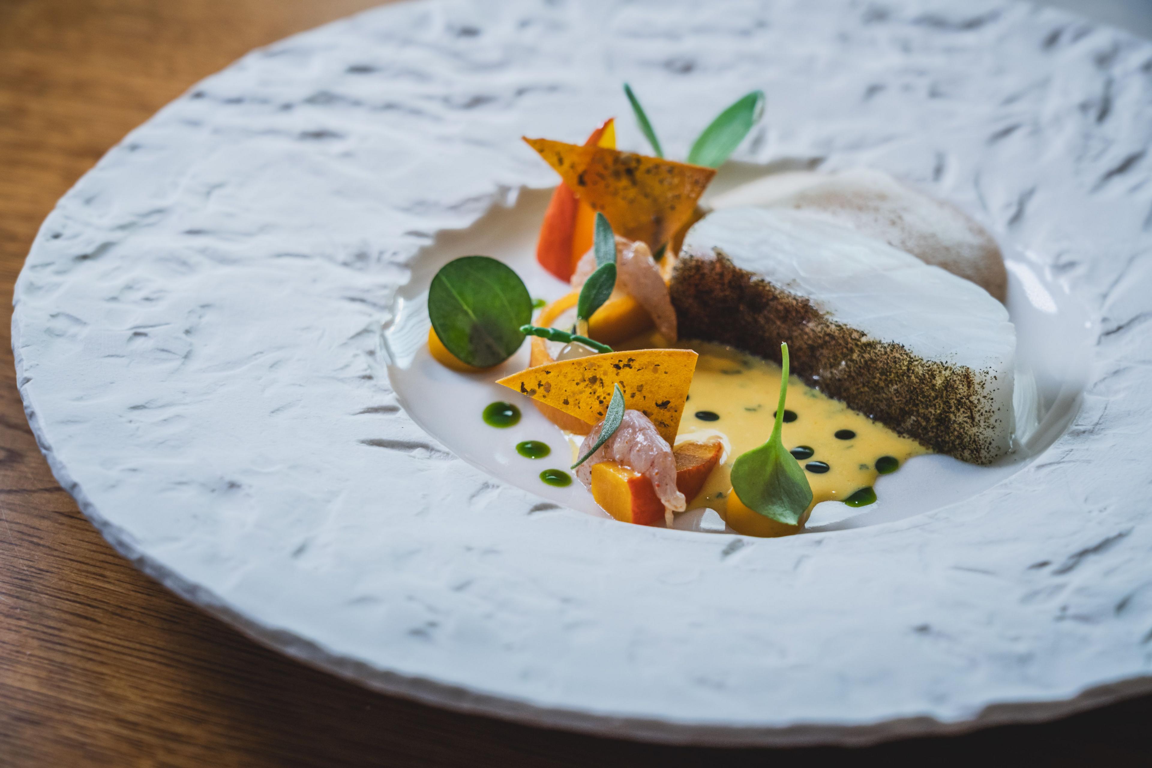 Wooden table with a white dish serving a colourful fish dish at Moor Hall