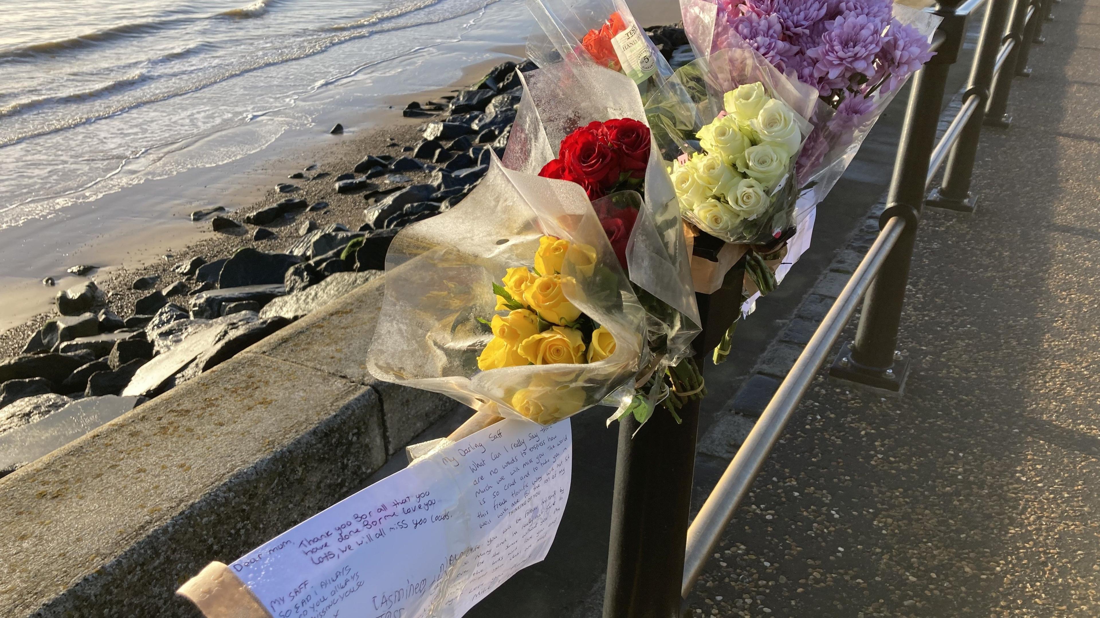 Floral tributes and cards on a barrier next to rocks and the sea