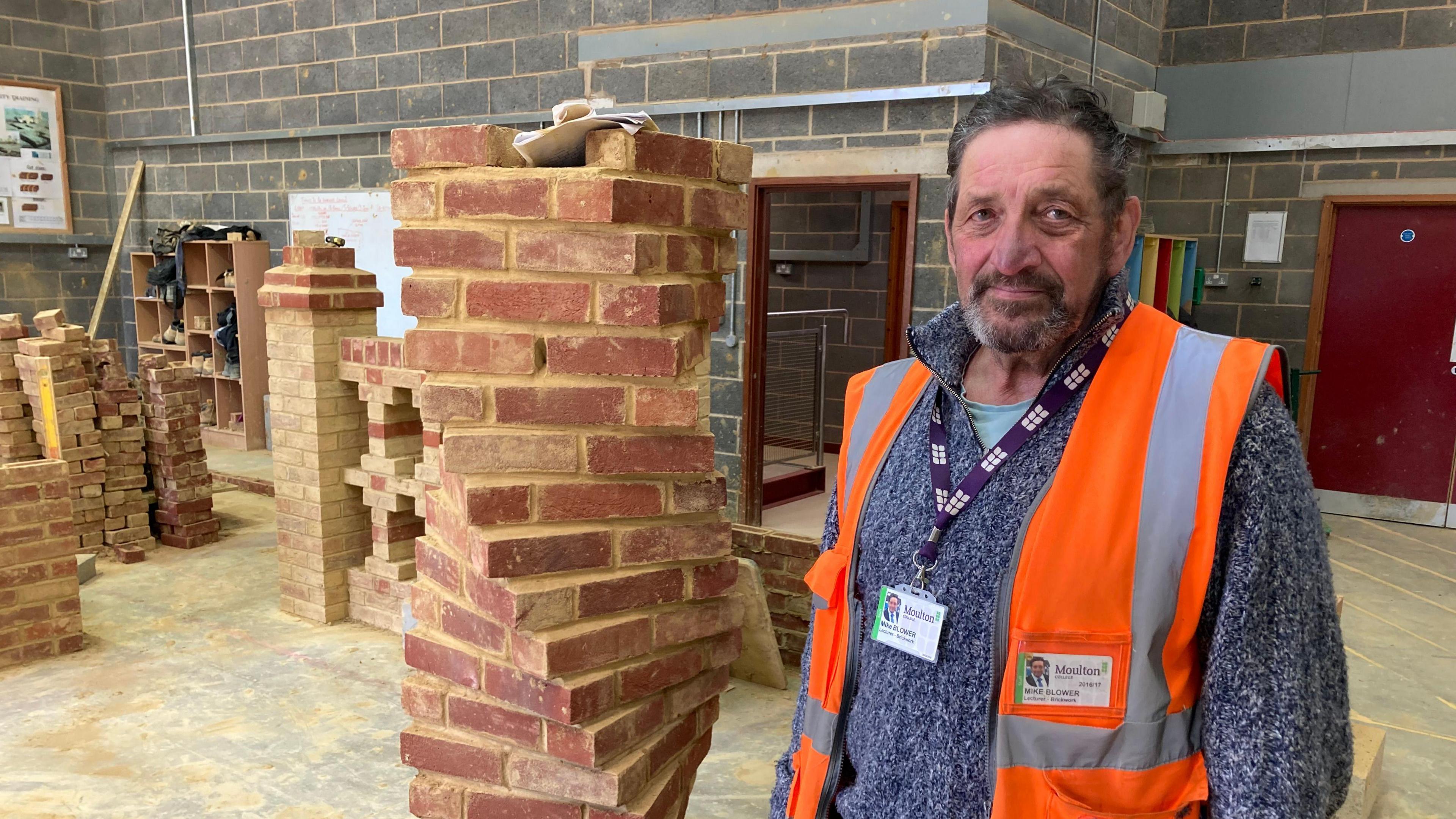 Man in orange high viz jacket stands next to pile of bricks