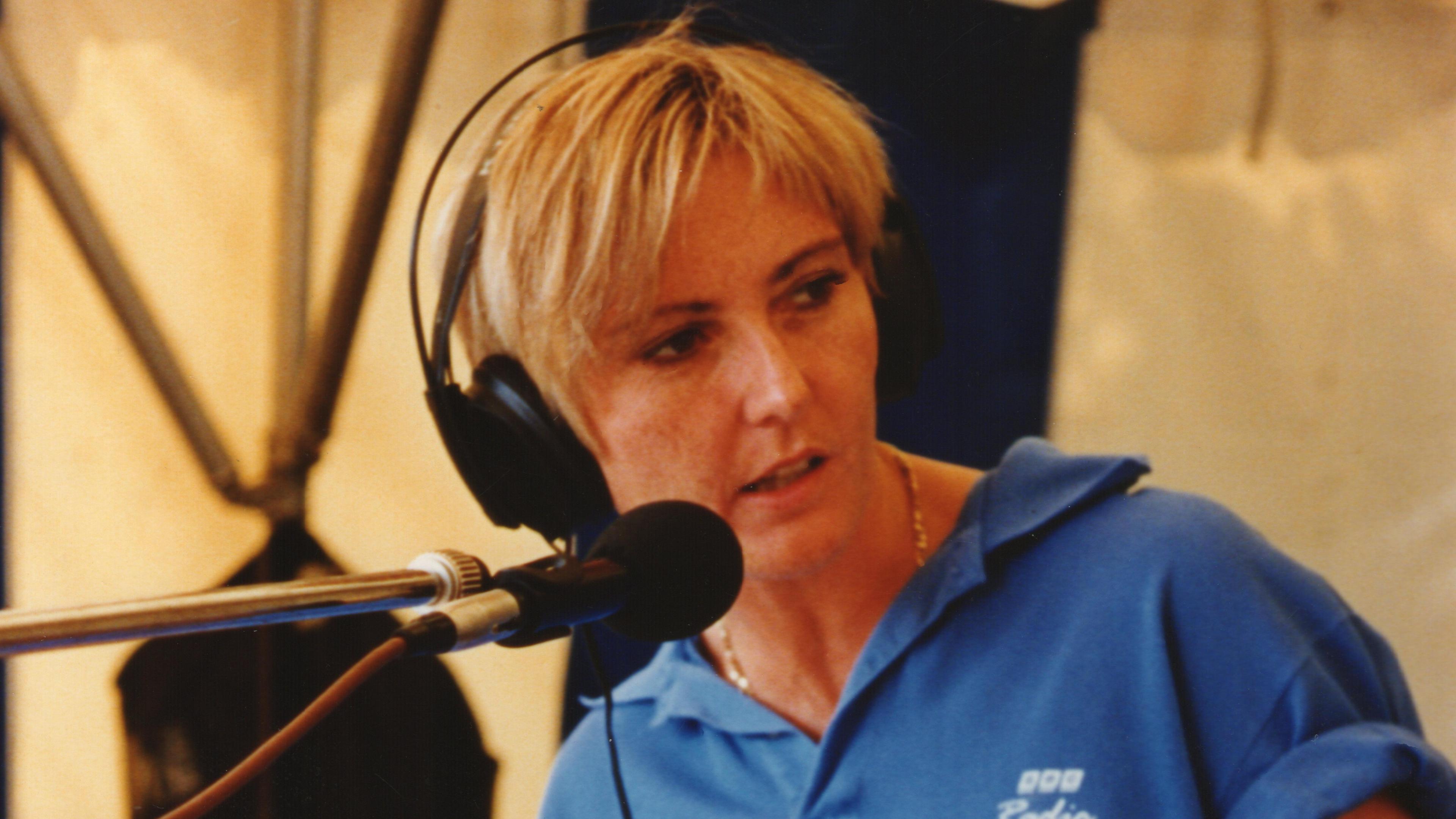 Pam Spriggs wearing headphones and a blue polo shirt speaks into a microphone.