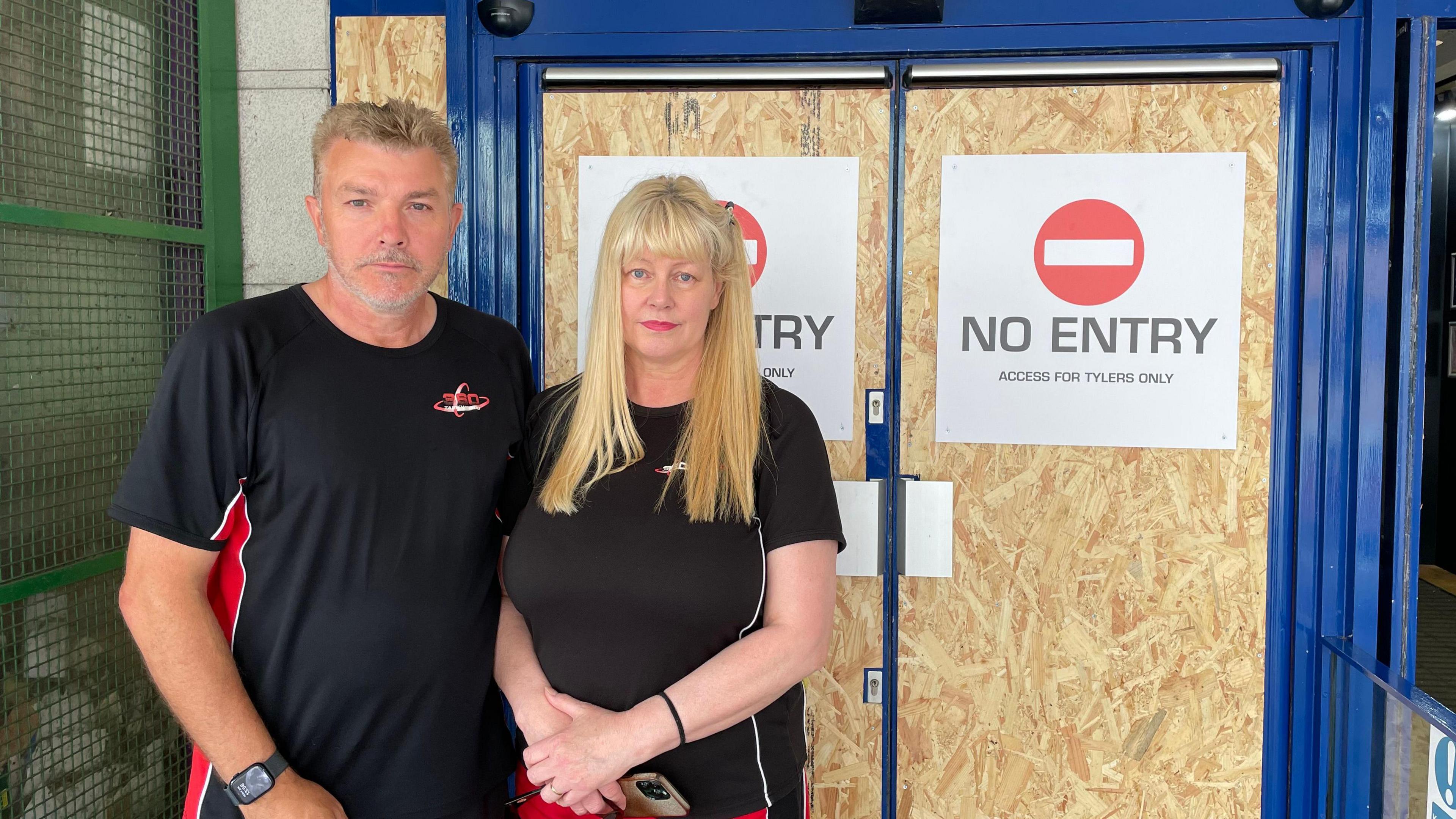 Sean and Julie Hutton stand before doors with boards on