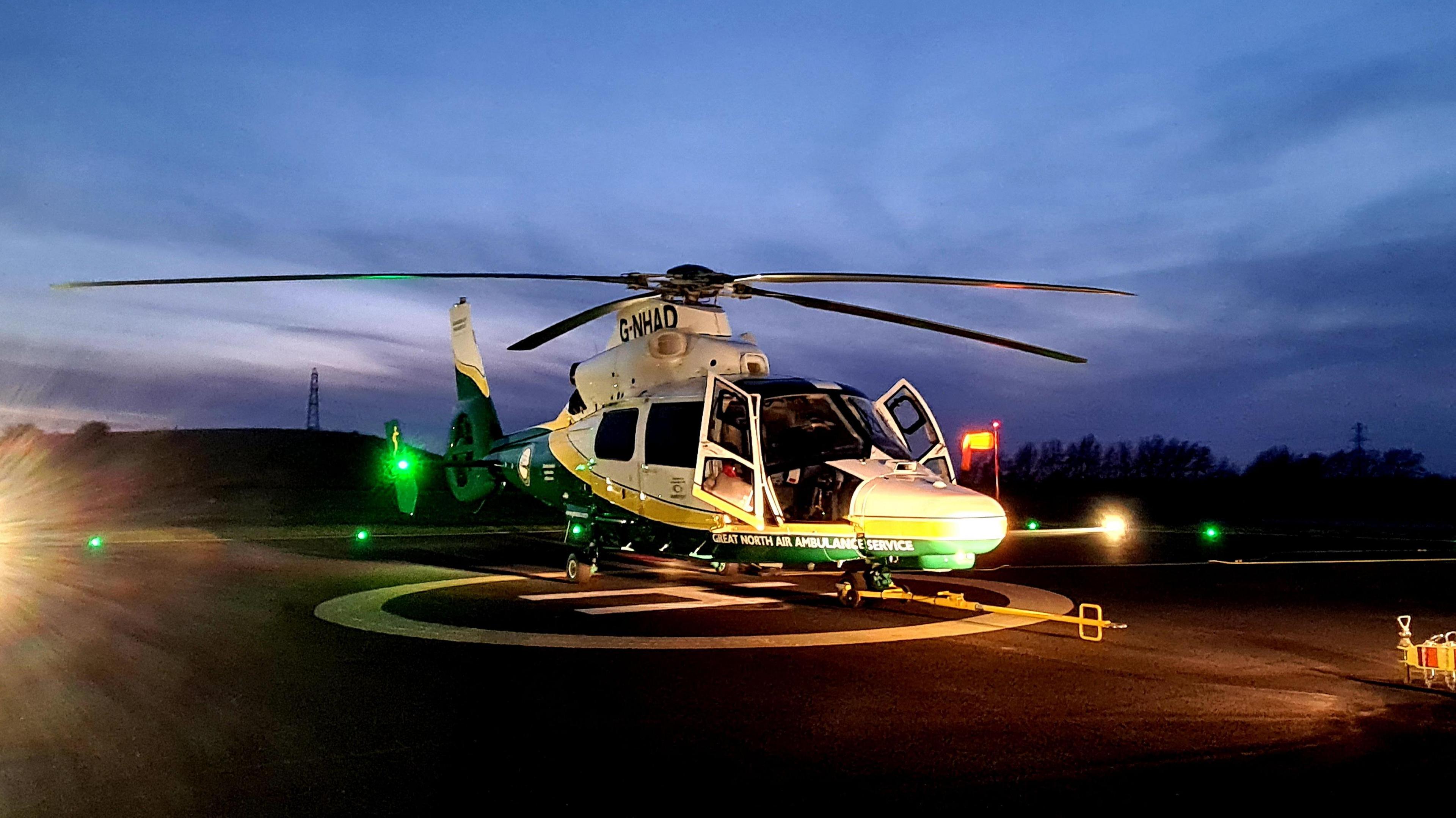 A Great North Air Ambulance sits on a helipad. It is dusk and there is blue sky. 