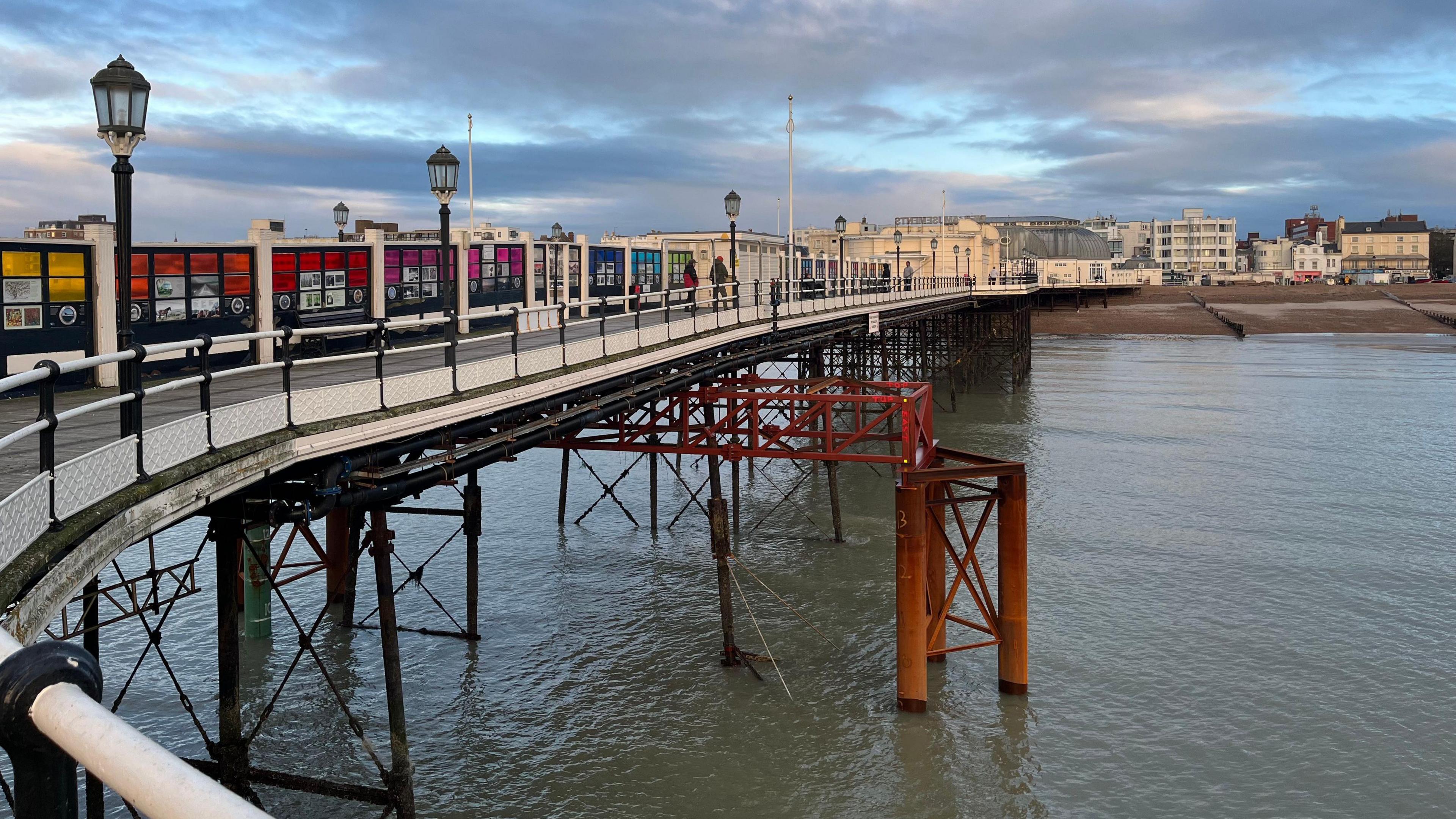 A red steel metal truss which is supporting the pier. It has three legs on either side which go into the ocean