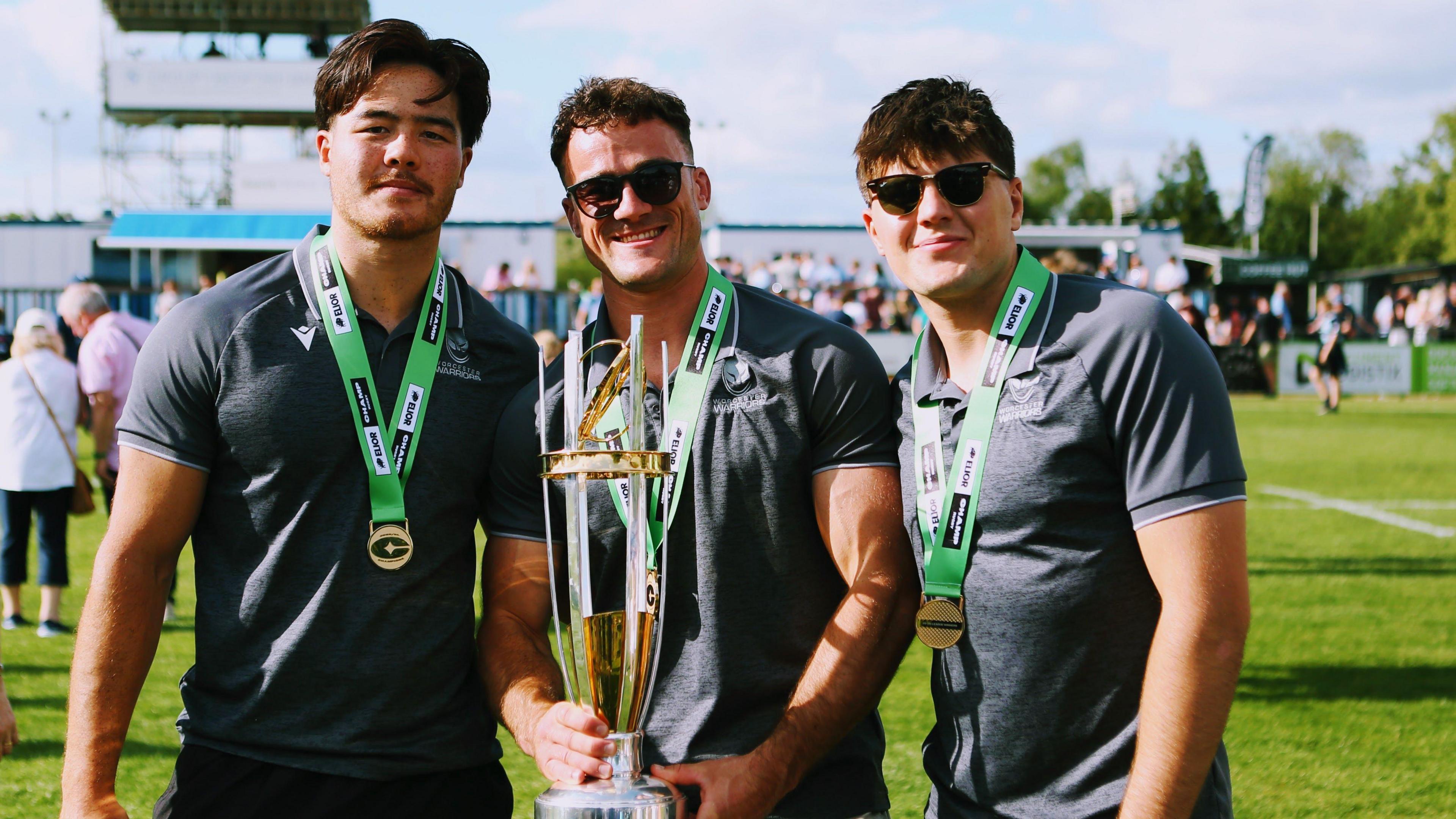 Three Worcester Warriors players celebrate winning the Champ Rugby title with the middle player Will Trewin holding the trophy 