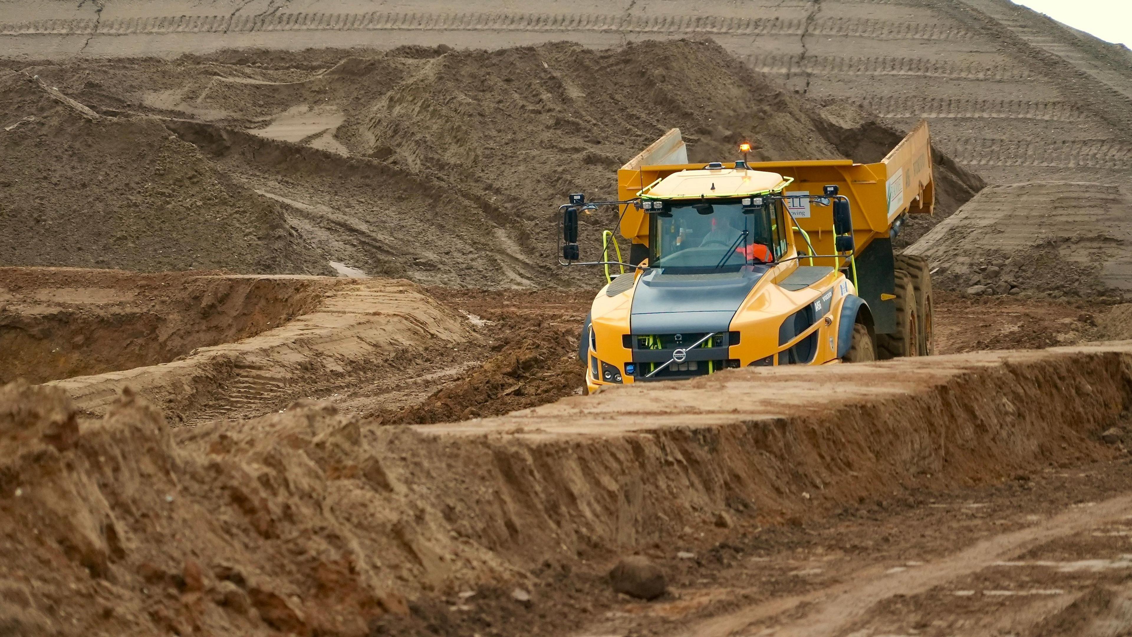 A large yellow earth-moving lorry with a mound of soil in the background