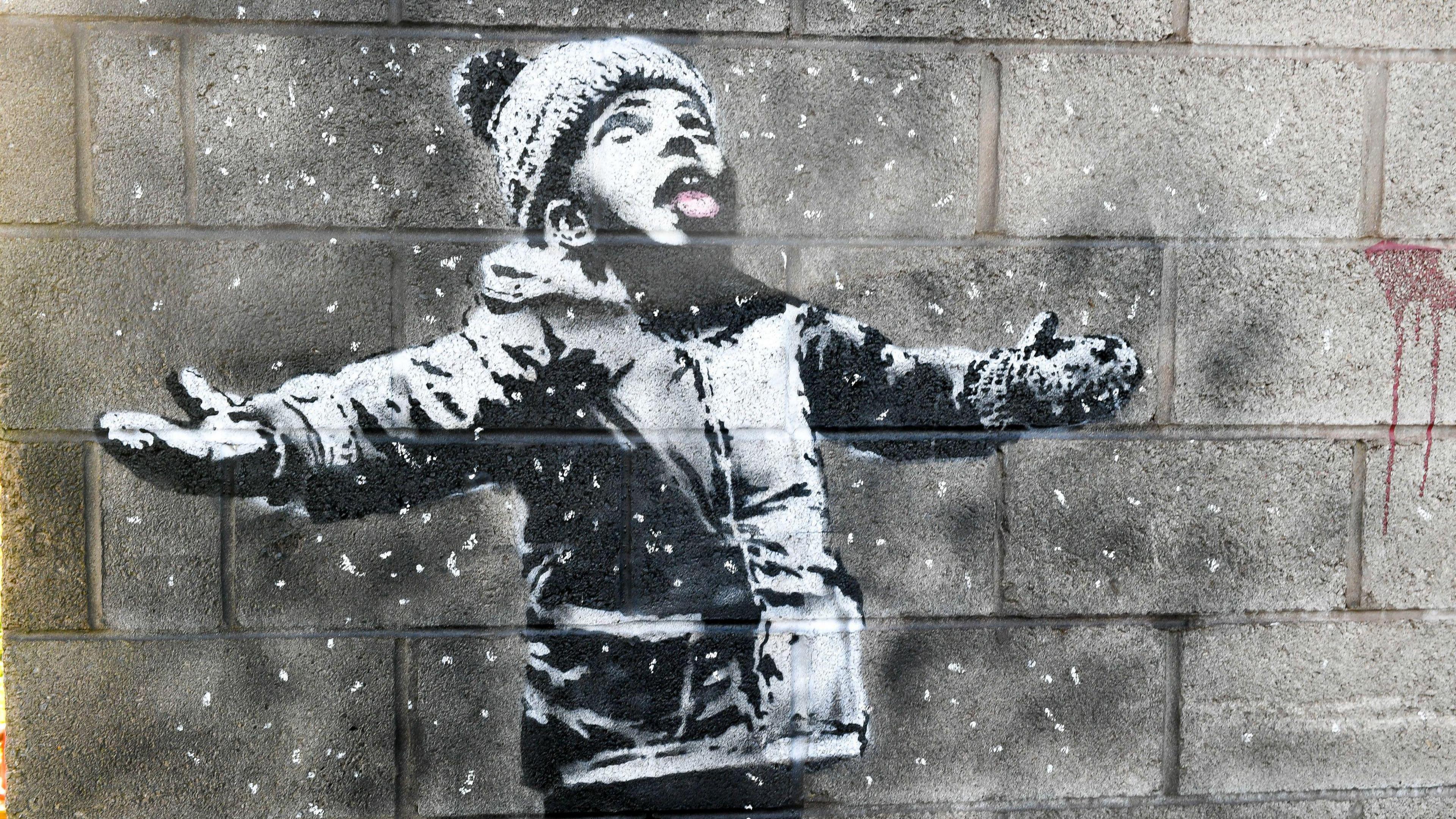 A lack and white mural of a small boy wearing a woolly hat, looking up with his mouth open, catching snowflakes
