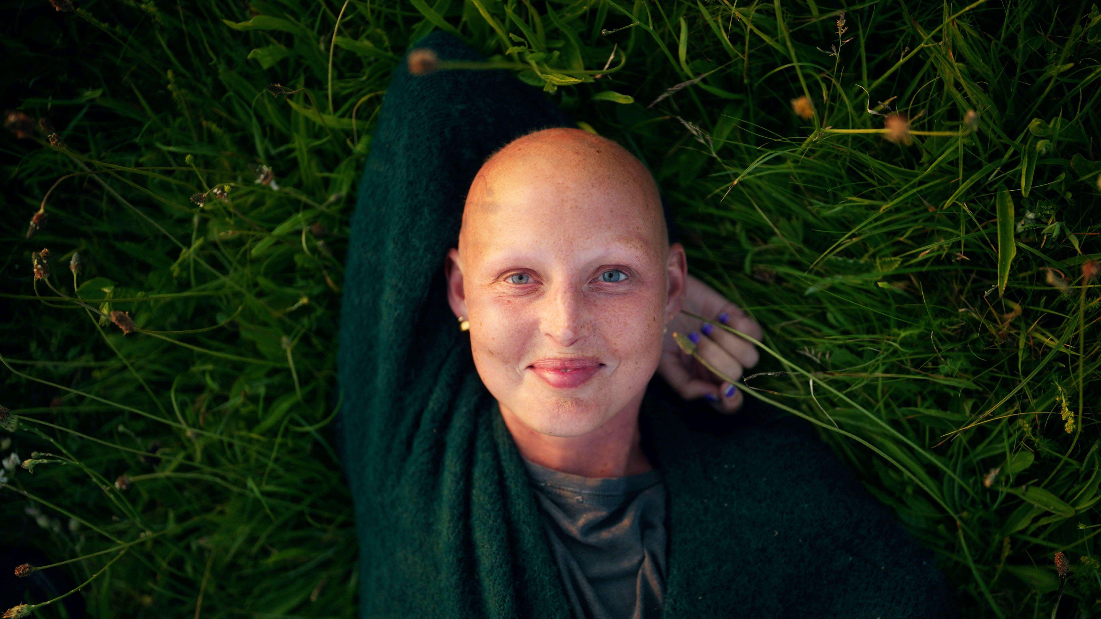 Kris Hallenga lies on her back on the grass. She is resting her head on her arm. Kris is wearing a green top and is smiling. 