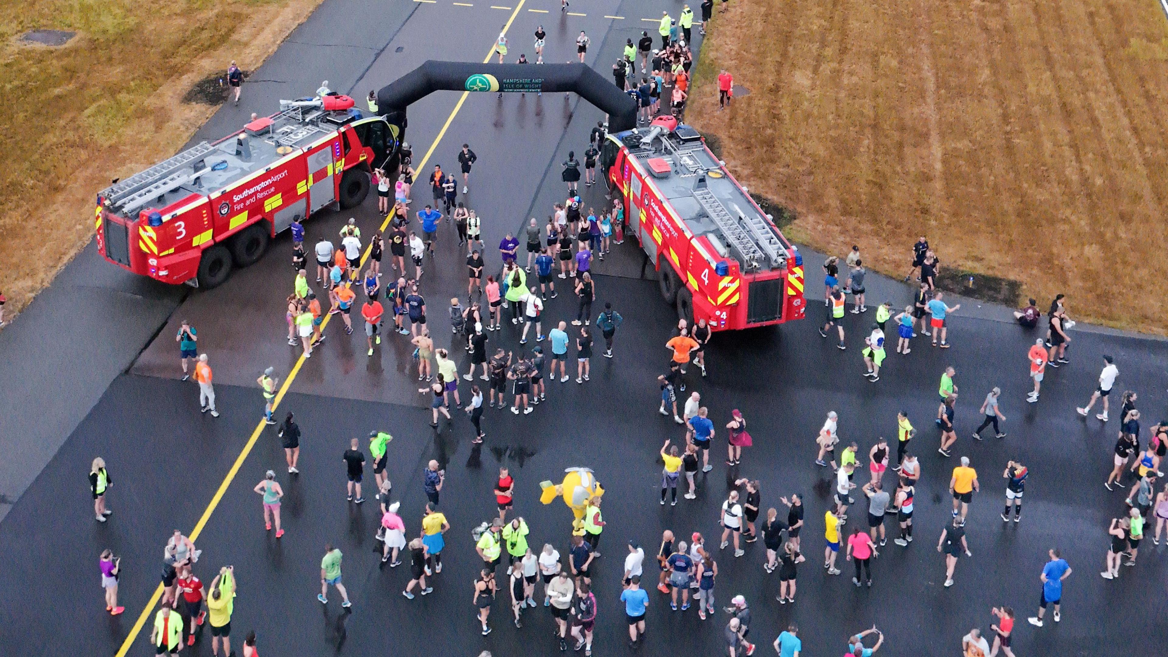 crowds of runners gathered on the runway with the inflatable finish line in vision and two fire engines on the side of the finish