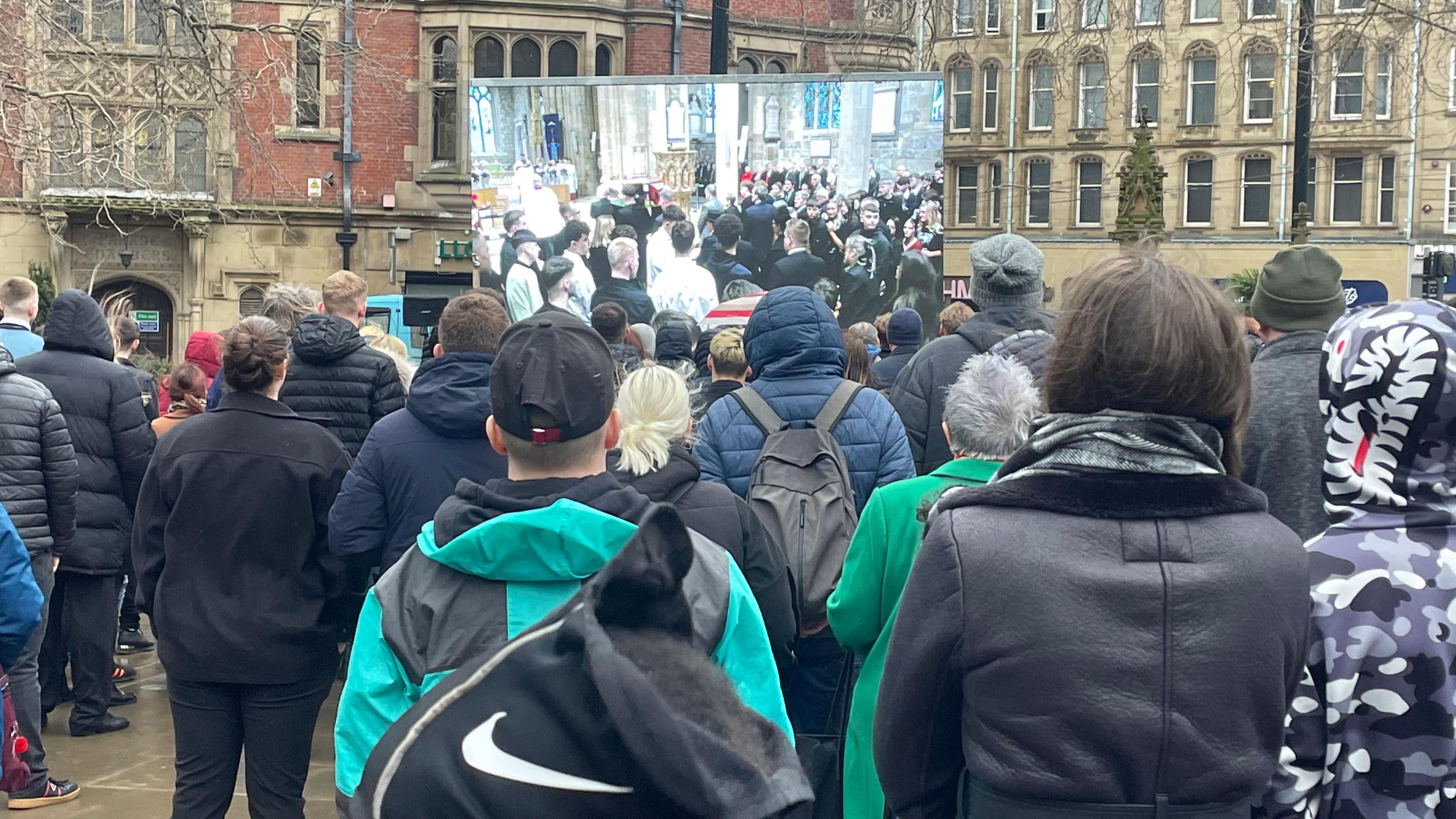 People watching the Harvey Willgoose funeral on a big screen outside 