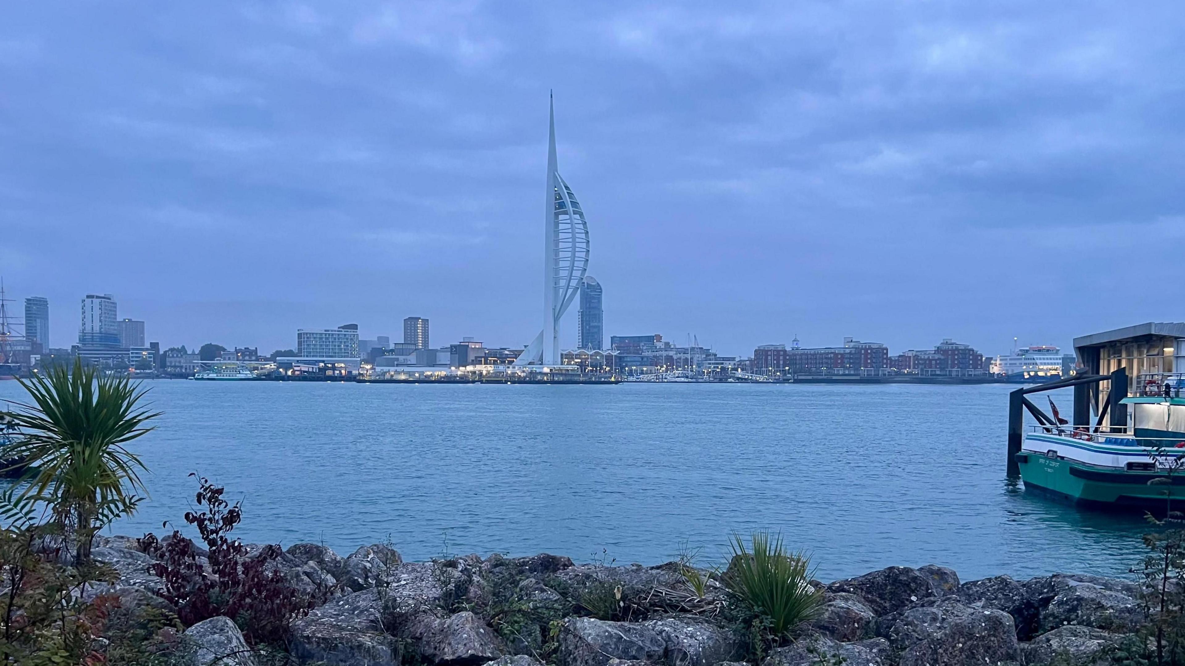 Portsmouth's skyline seen behind a large body of water and under grey clouds, with the Spinnaker Tower in the centre