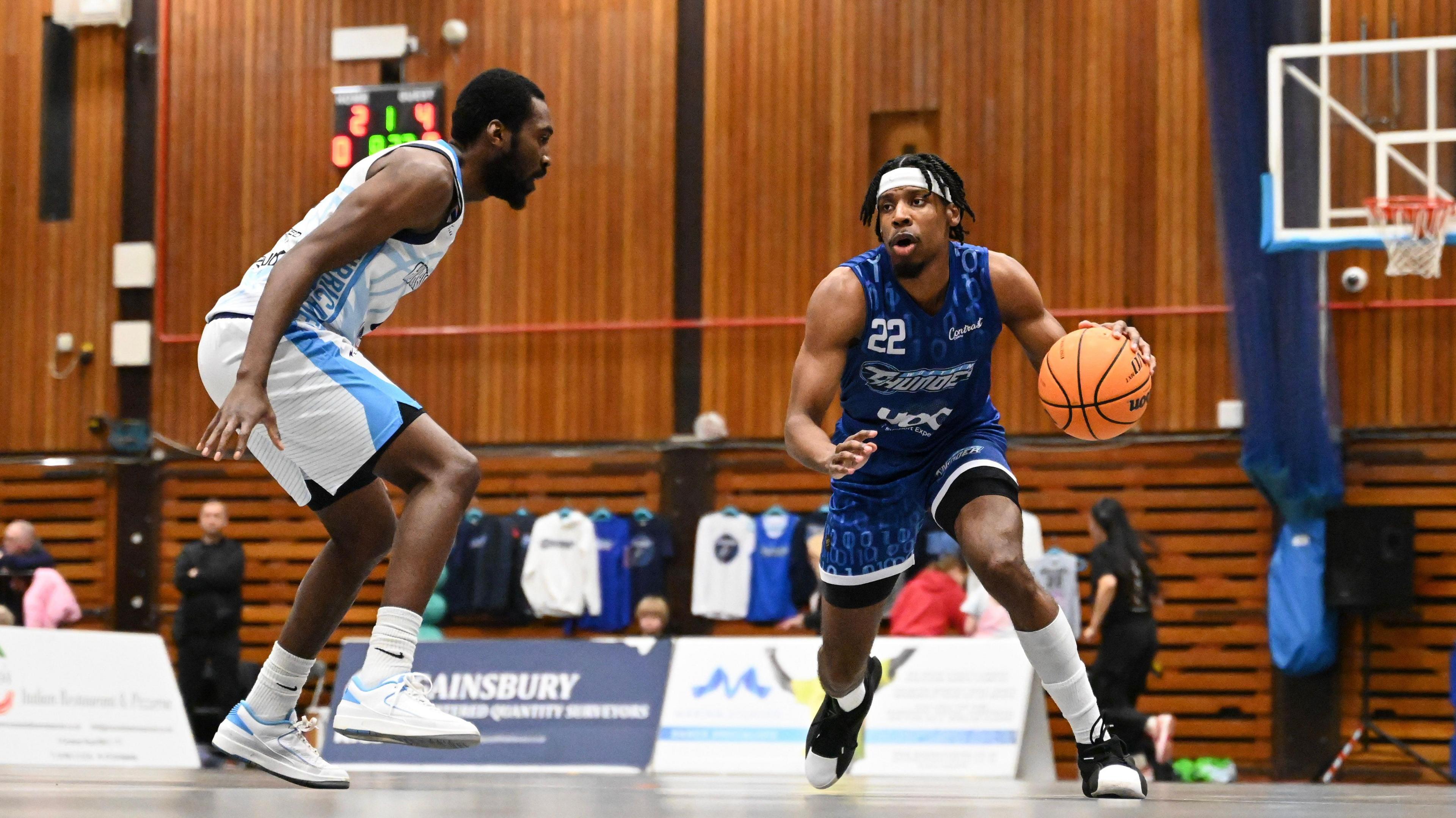 A person in a blue basketball kit drilling a basketball towards a person in a white basketball kit. The blue kit says "Worthing Thunder" on the front.