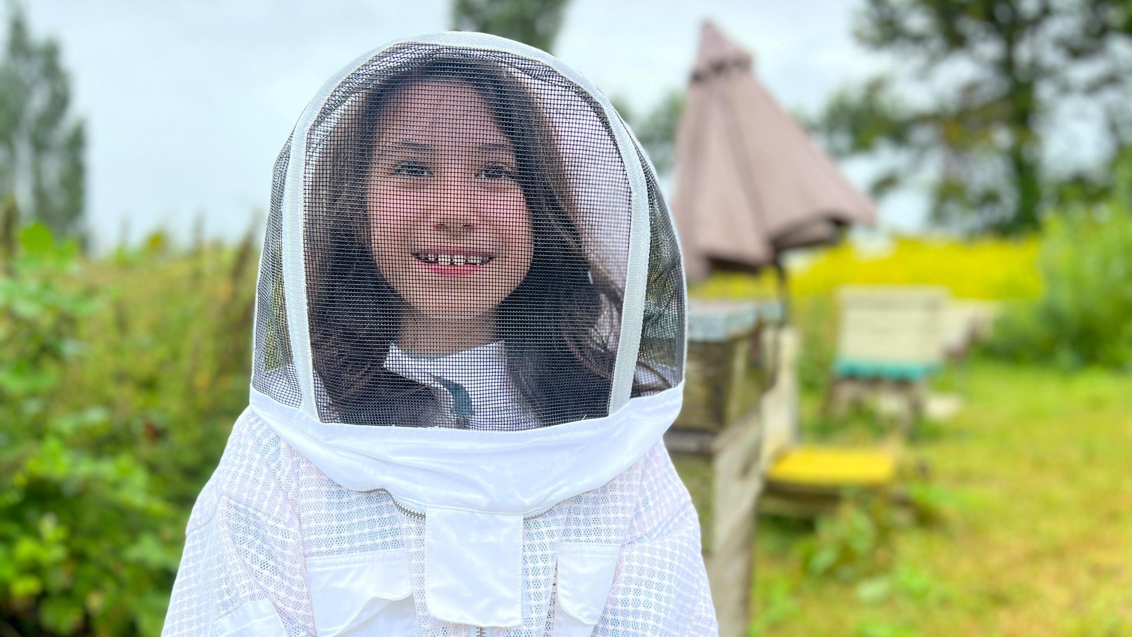 Adriana smiles at the camera as she wears a beekeeper suit