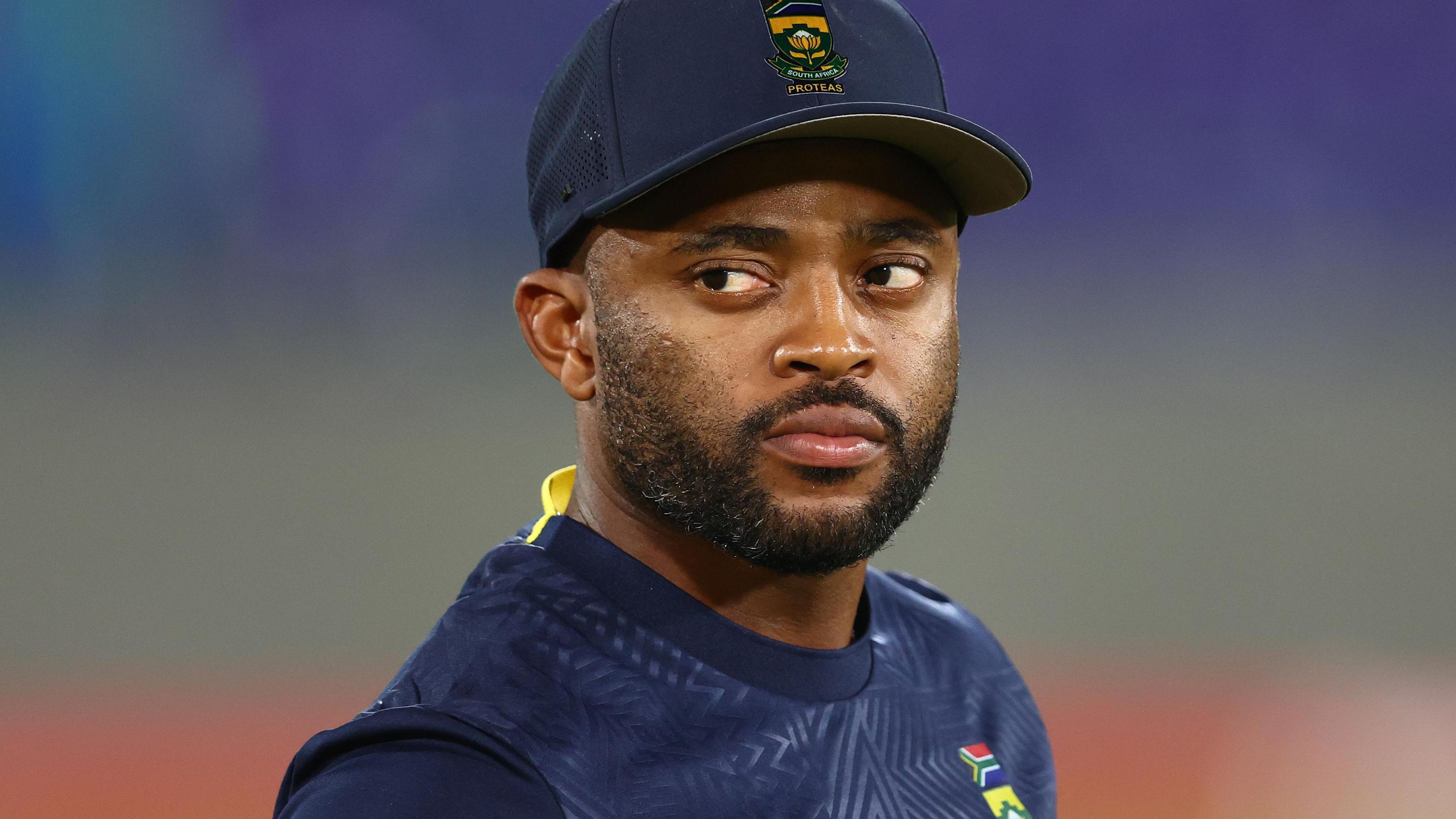 Temba Bavuma, wearing a dark blue South Africa cap and training shirt, looks to his right