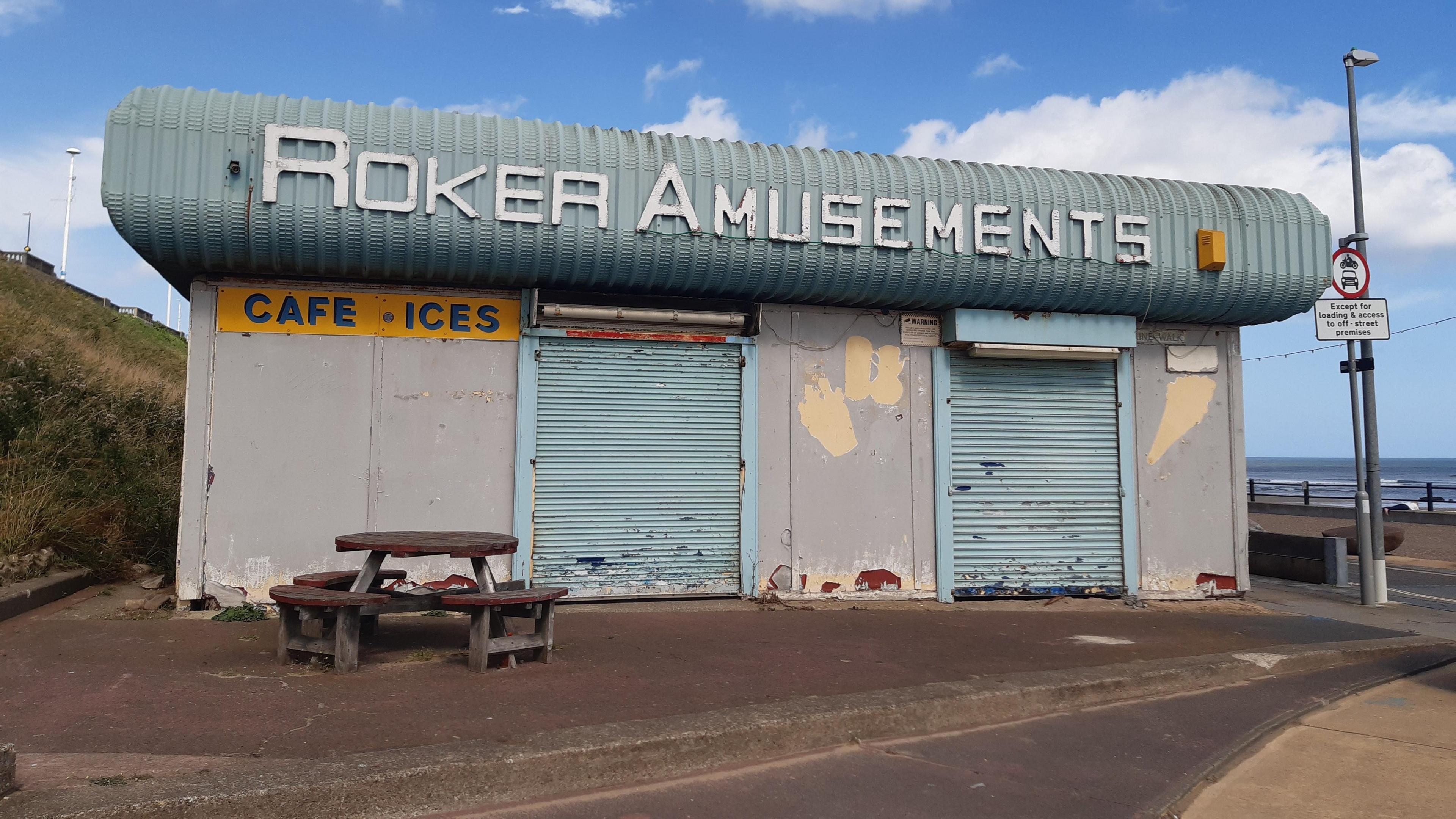 A picture of a rundown building with blue shutters and a sign saying Roker Amusements 