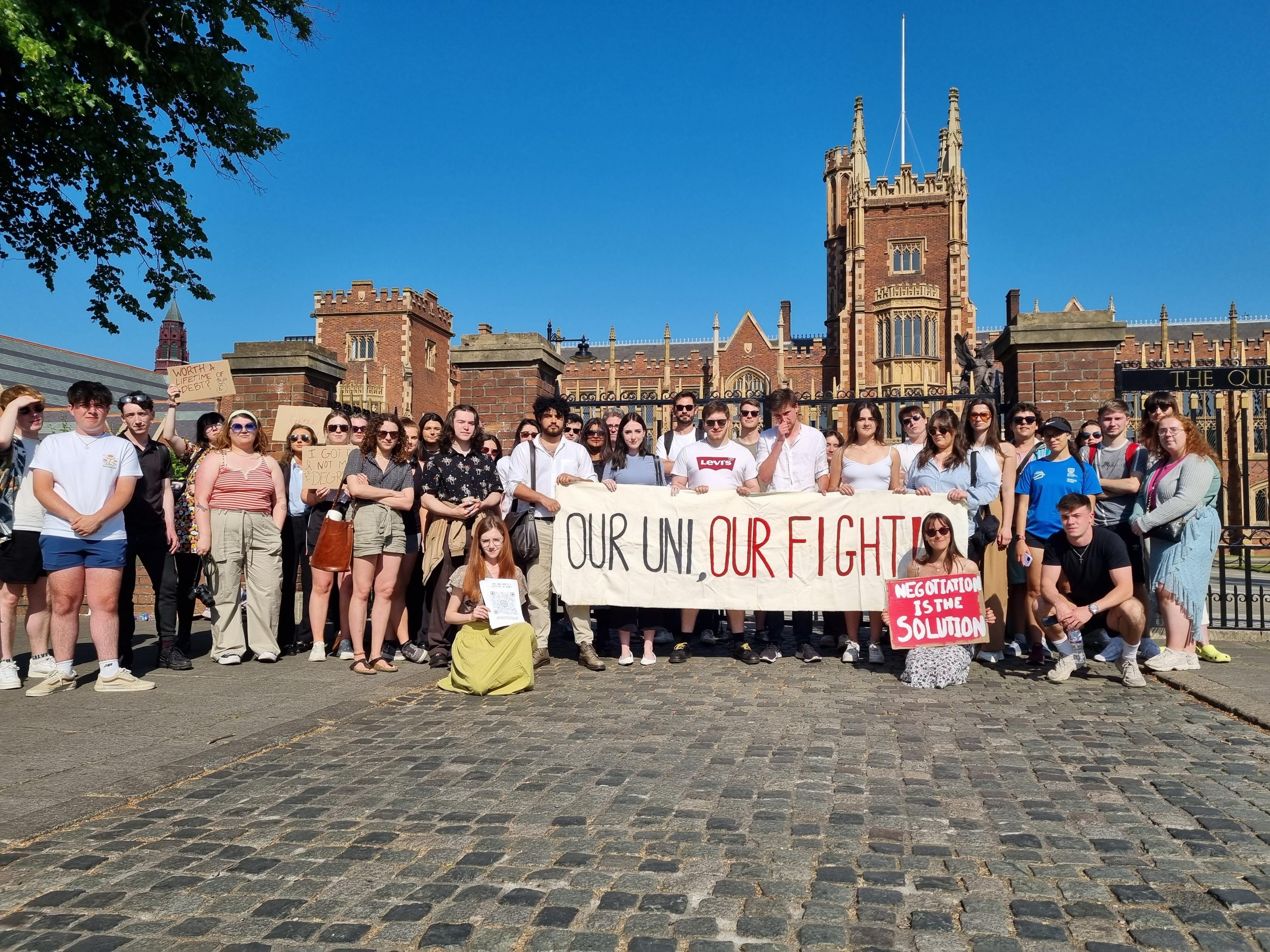 A group of students gathered outside Queen's University Belfast holding a signed reading 'our uni, our fight'