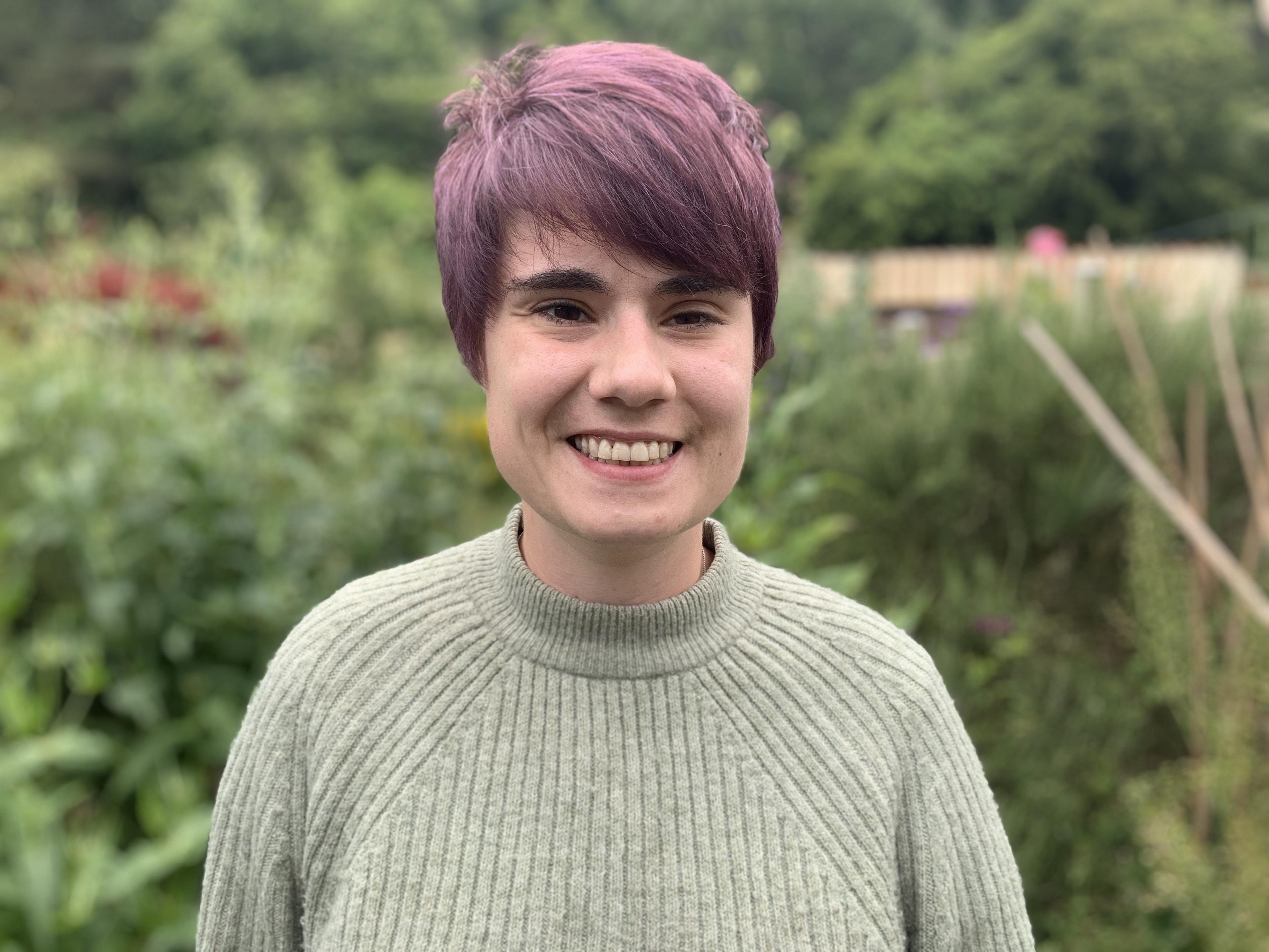 A lady with short hair, wearing a green jumper standing in her garden.