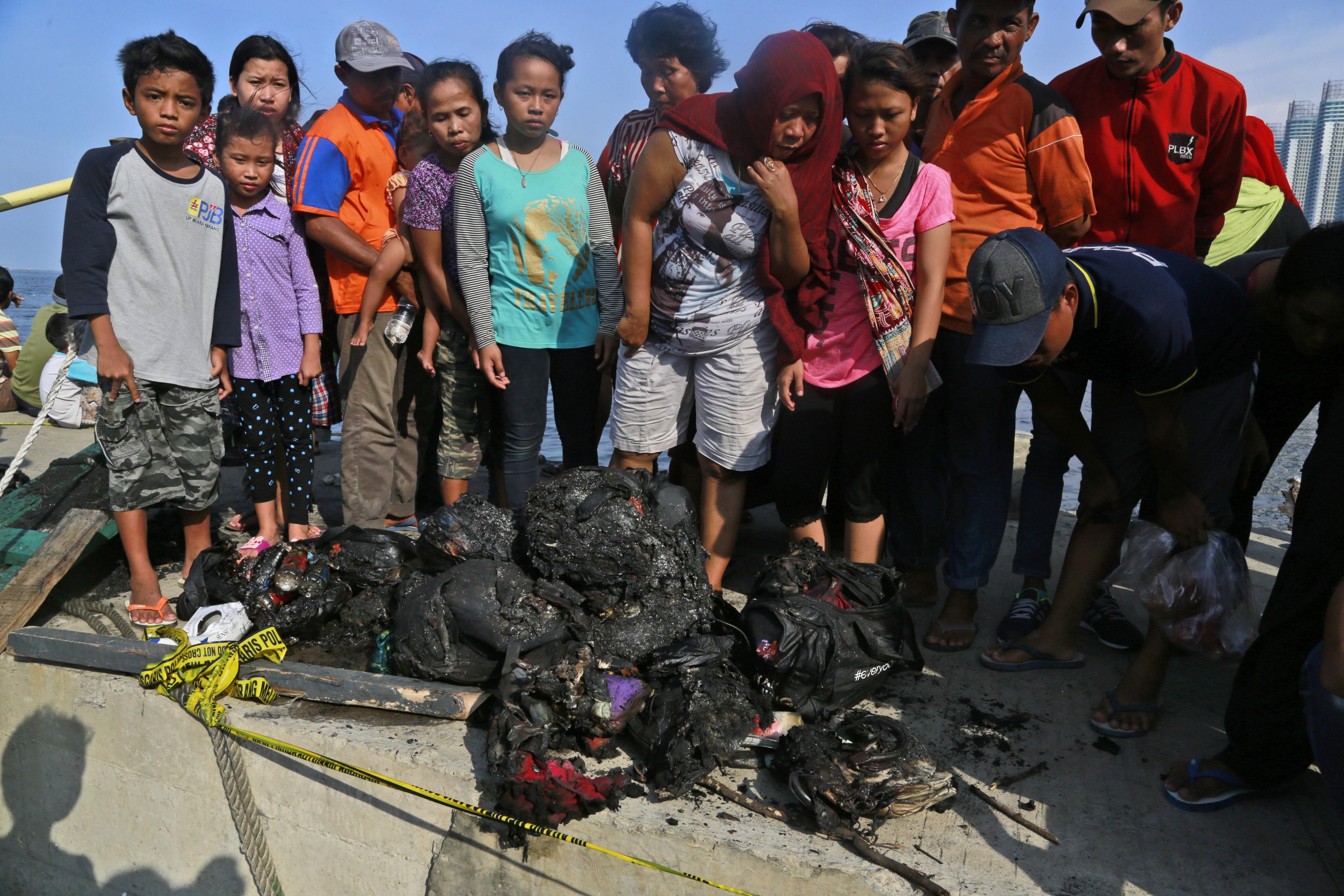 People inspect charred personal belongings of the passengers of a ferry that caught fire off the coast of Jakarta, at Muara Angke Port in Jakarta, Indonesia, Sunday, Jan. 1, 2017.