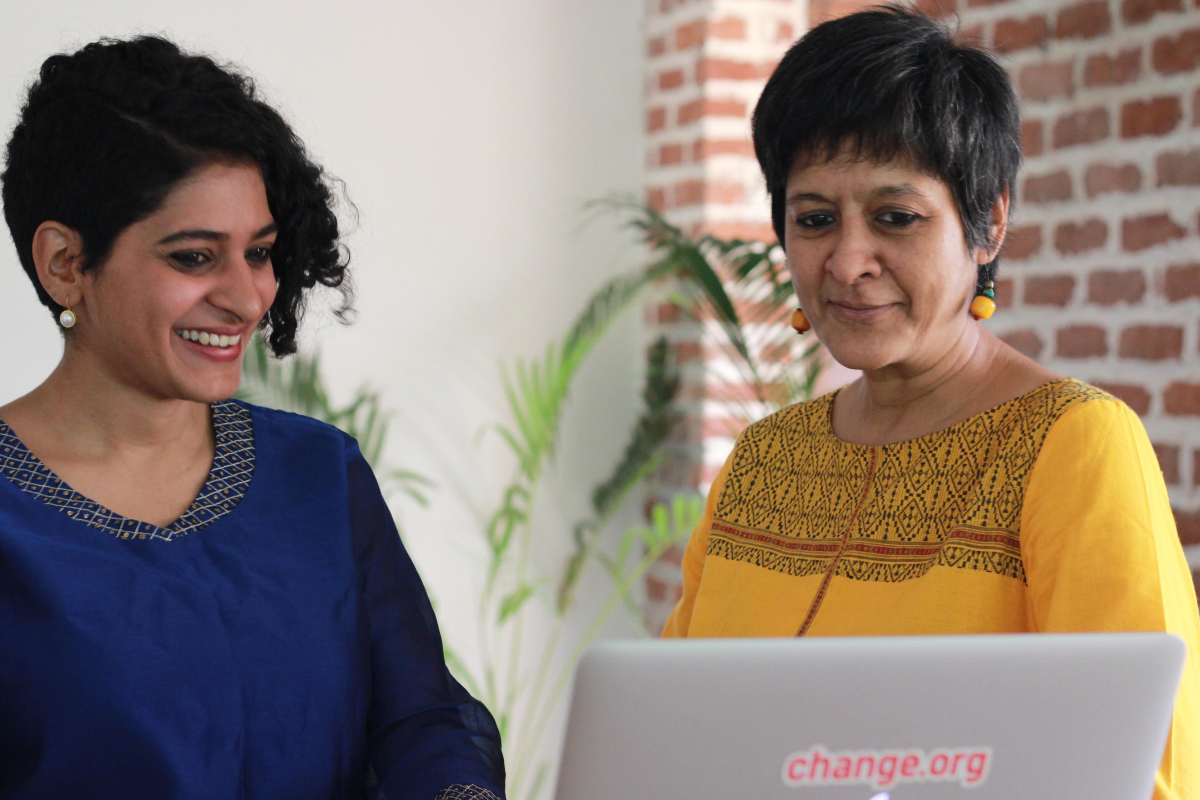 Preethi Herman and Masooma Ranalvi look at a laptop smiling.