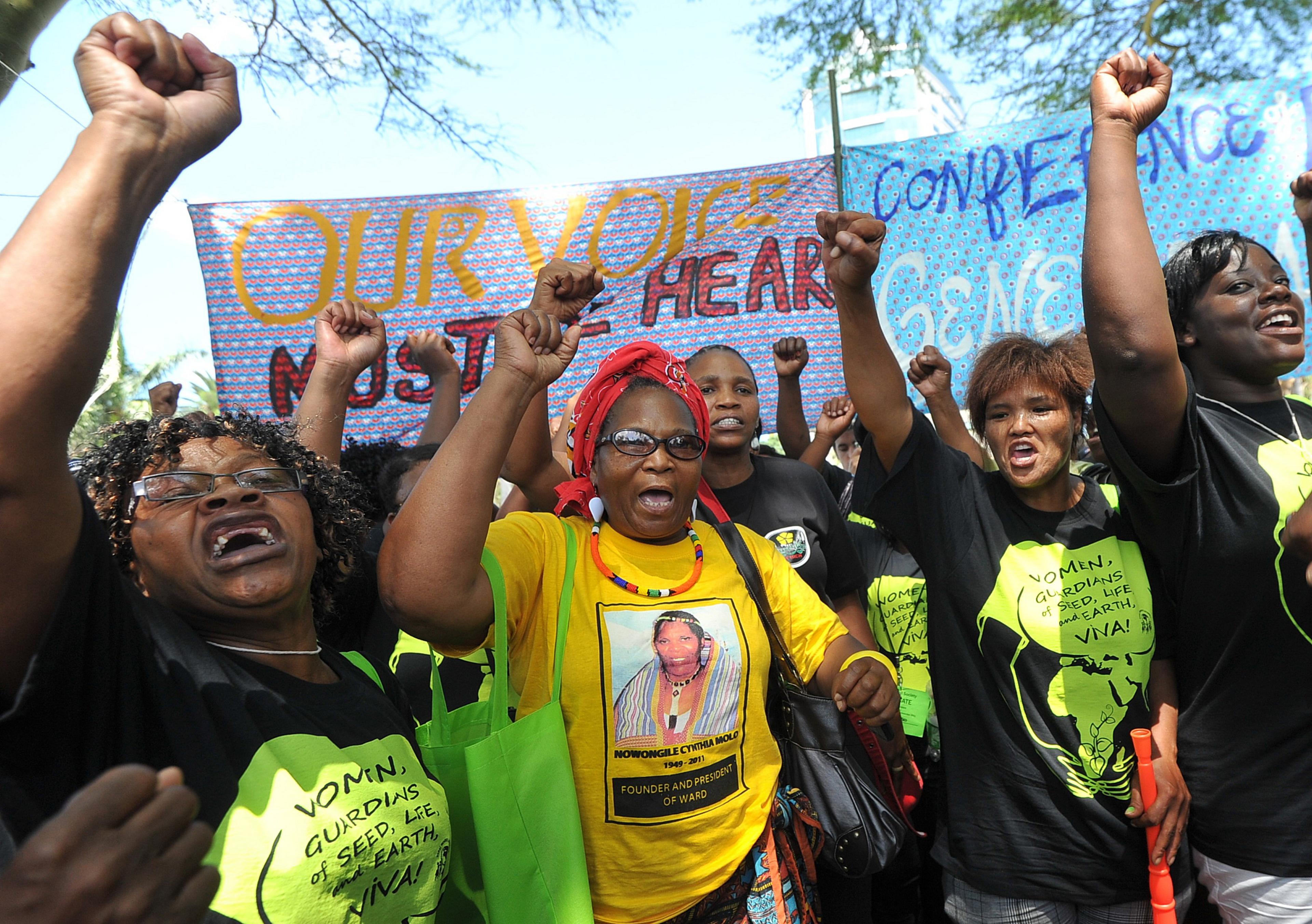 A group of women farmers with their fists raised, carrying protest banners