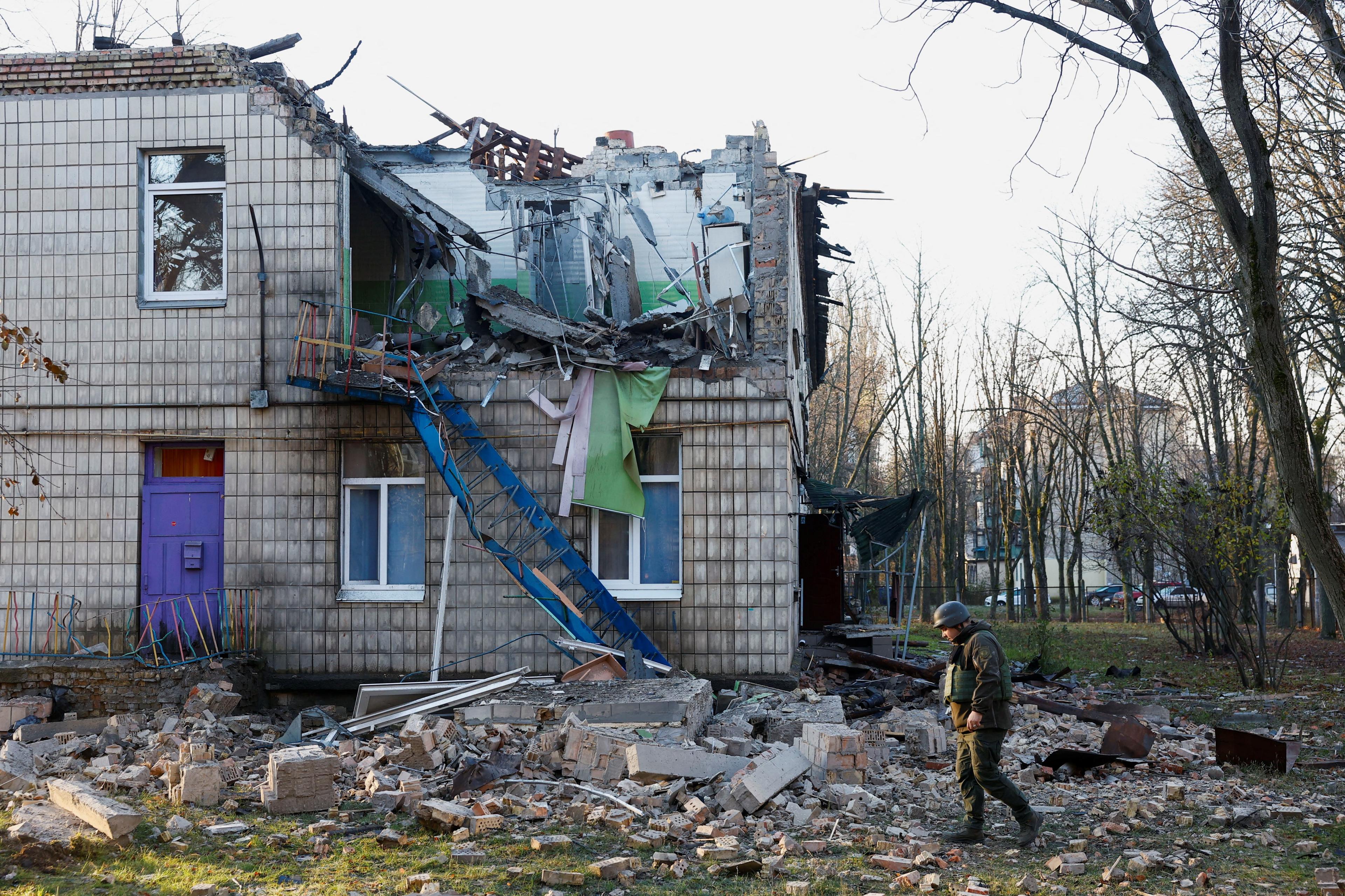 A police officer walks past a kindergarten that was heavily damaged by a drone strike. with a hollowed-out side.