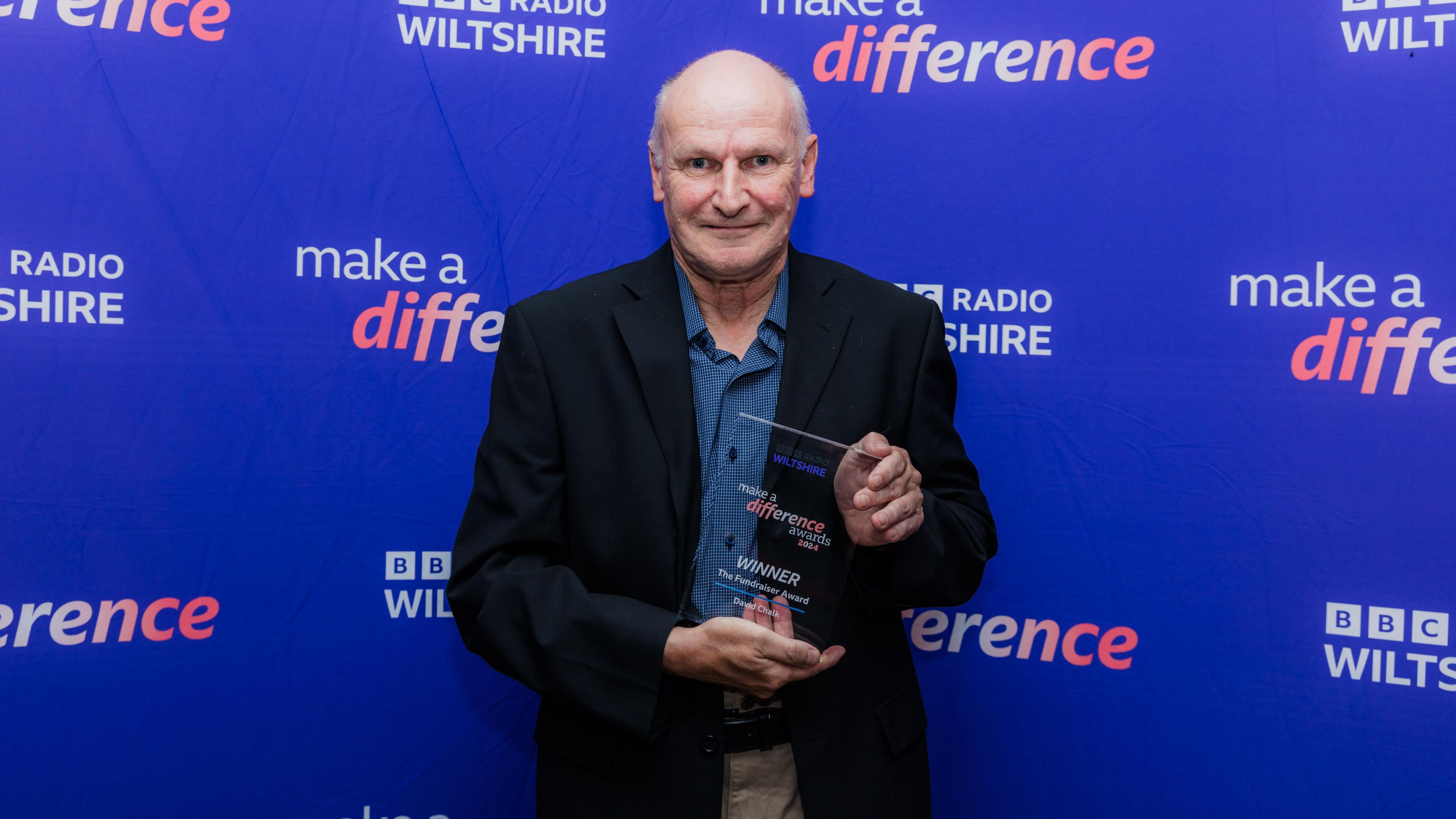 David Chalk with his glass award in front of the purple banner