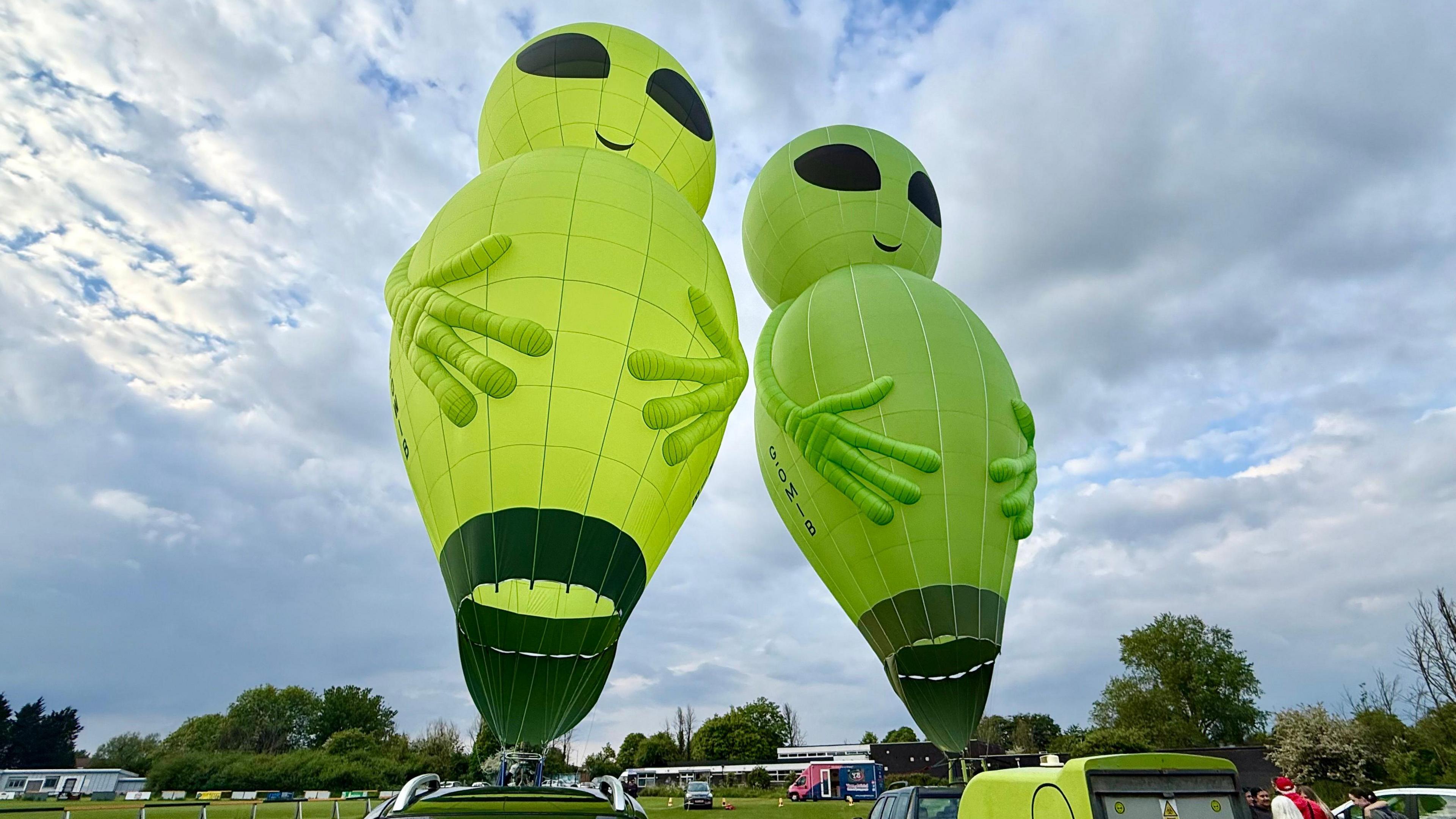 Two alien hot air balloons tethered to vehicles on a field.