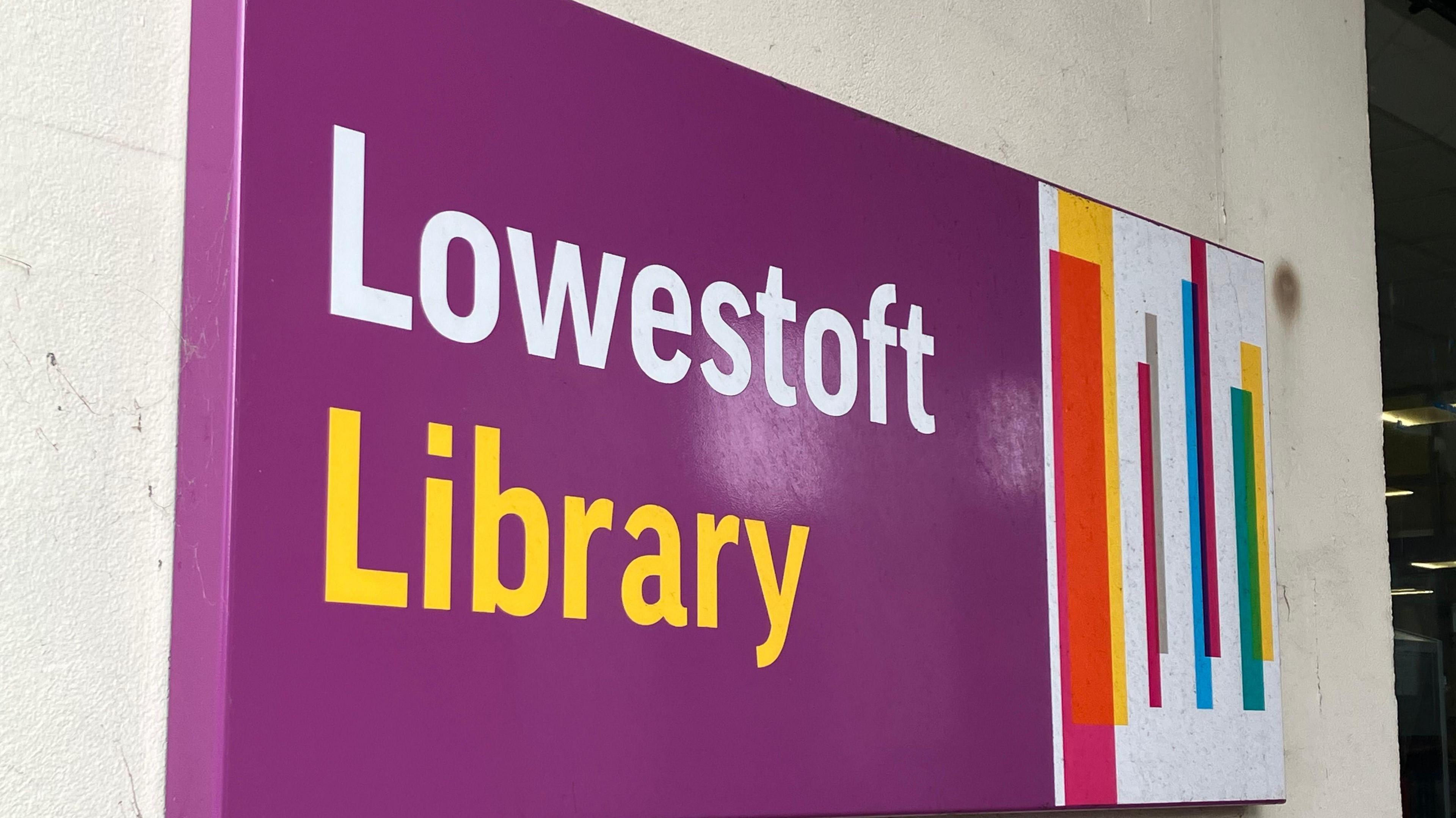 A purple sign with yellow and white lettering reading Lowestoft Library