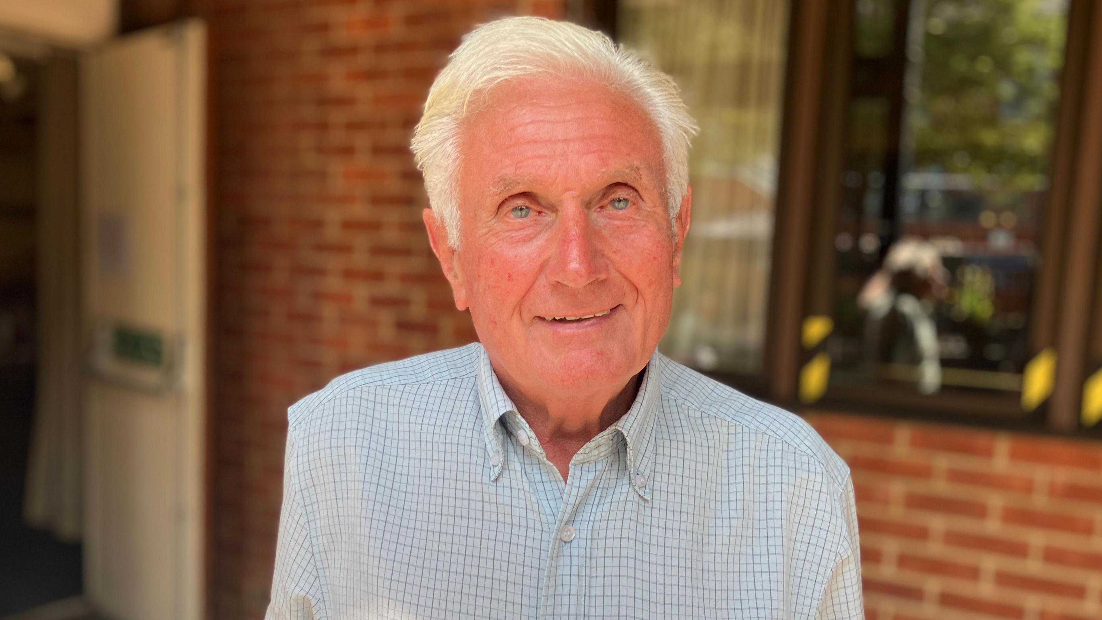 Rob Marshall has short white hair and is stood in front of the red-brick GF Social Club building.