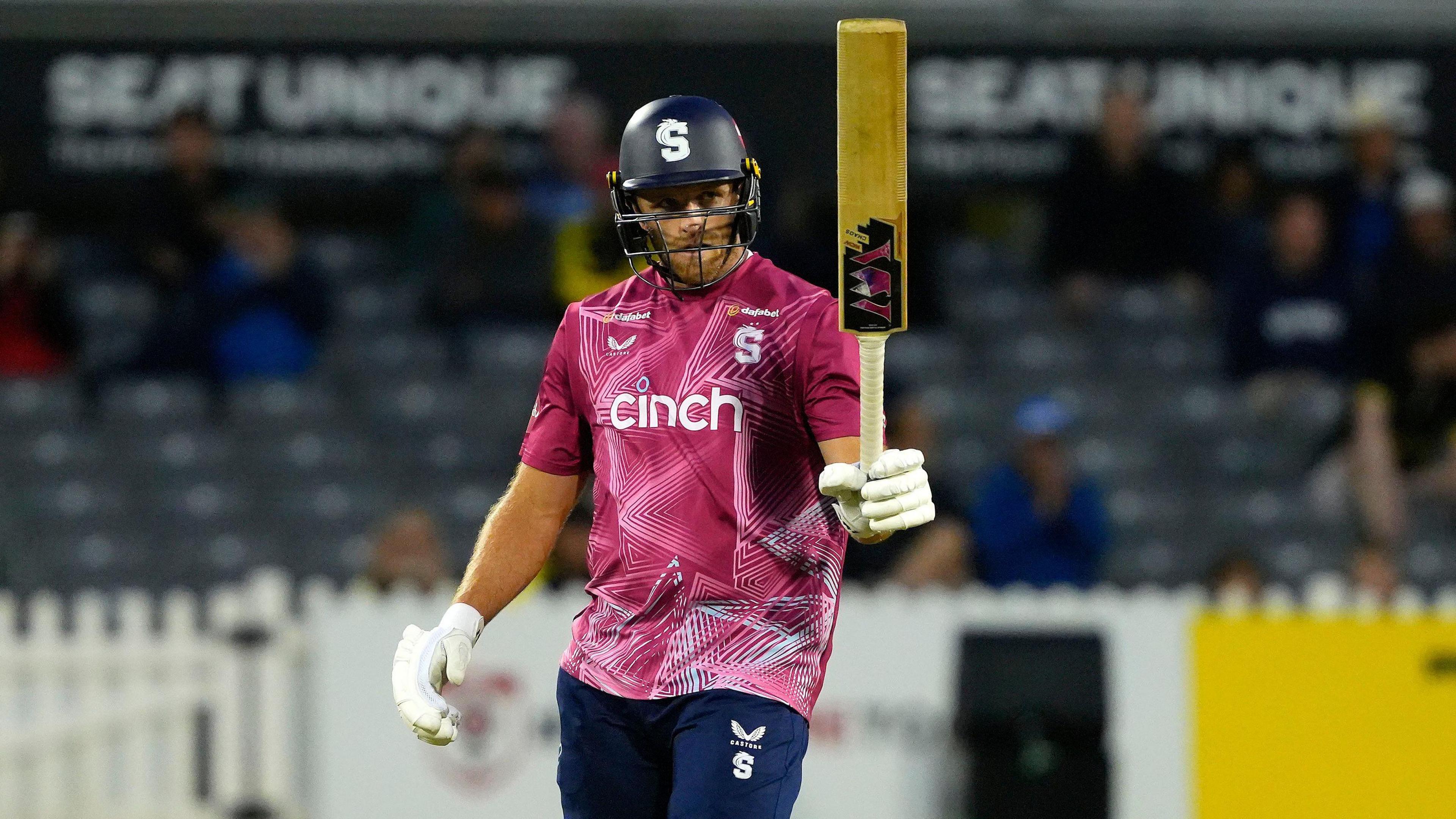 David Willey holding his bat aloft in his left hand after scoring a half-century for Northamptonshire Steelbacks