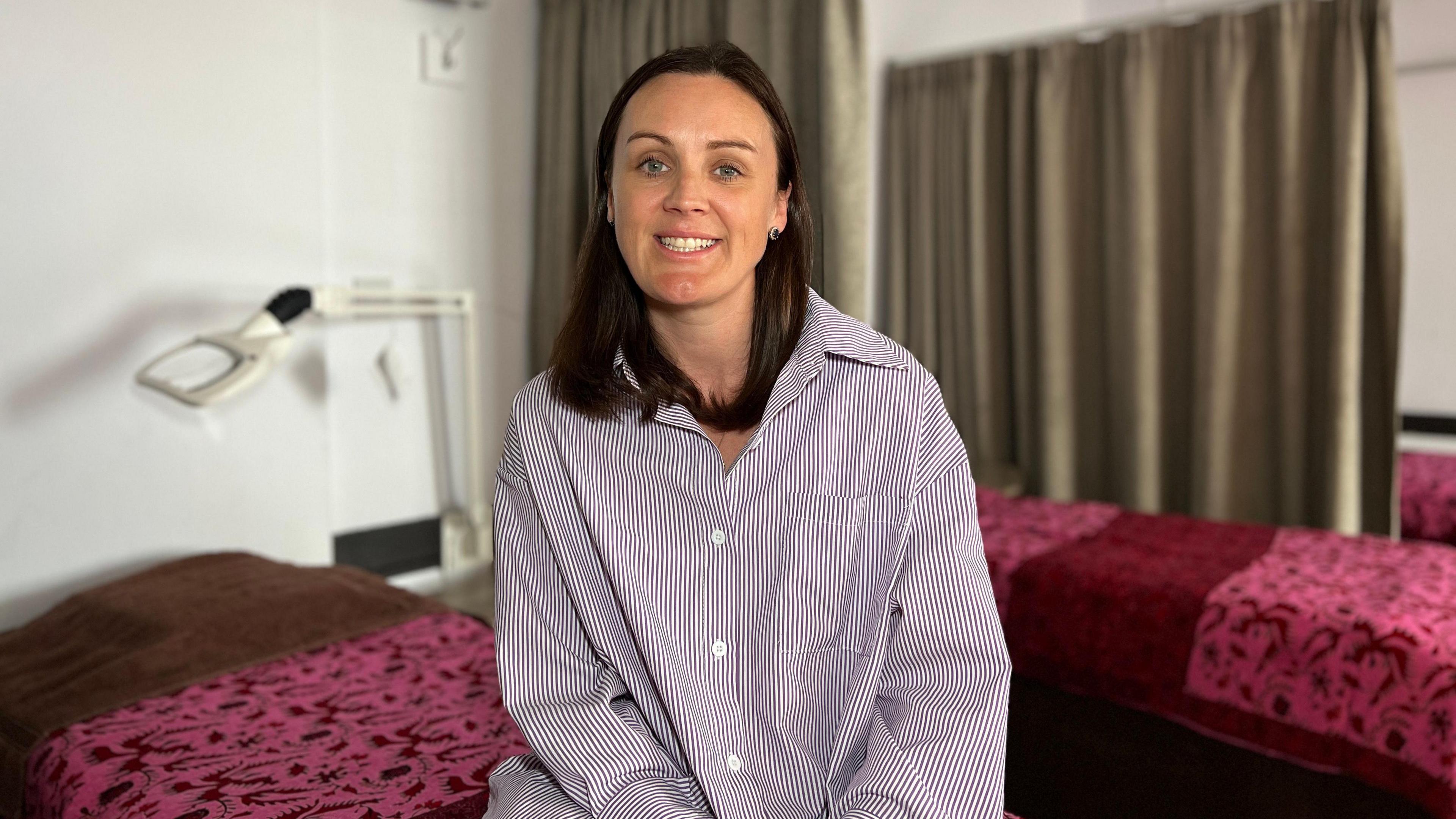 Steph sits on a massage bed and smiles at the camera