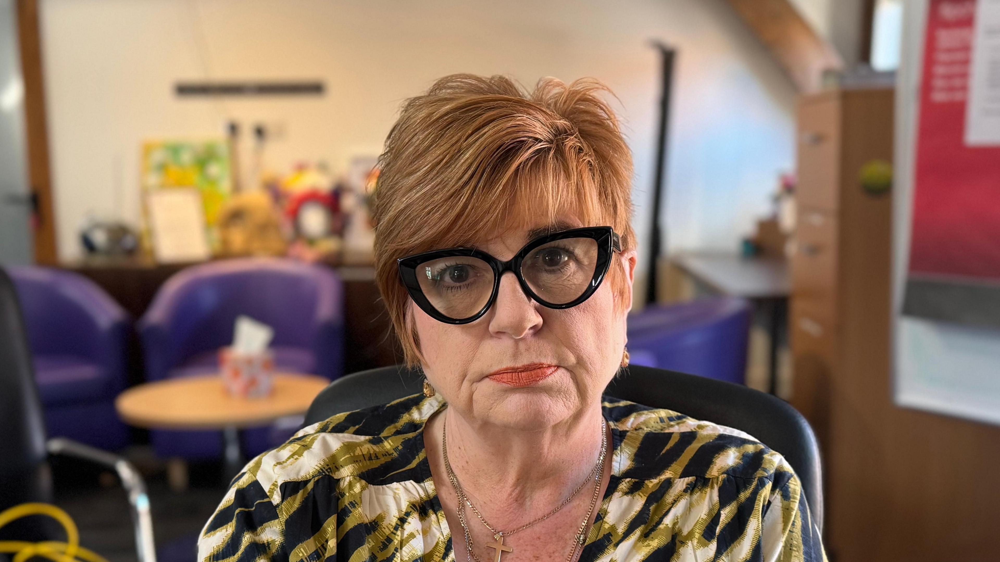 A head and shoulders image of Katherine Ahluwalia, principal operations manager for Suffolk's Restore Women's Aid. She is wearing black glasses and sitting in a black chair. She is staring into the camera.